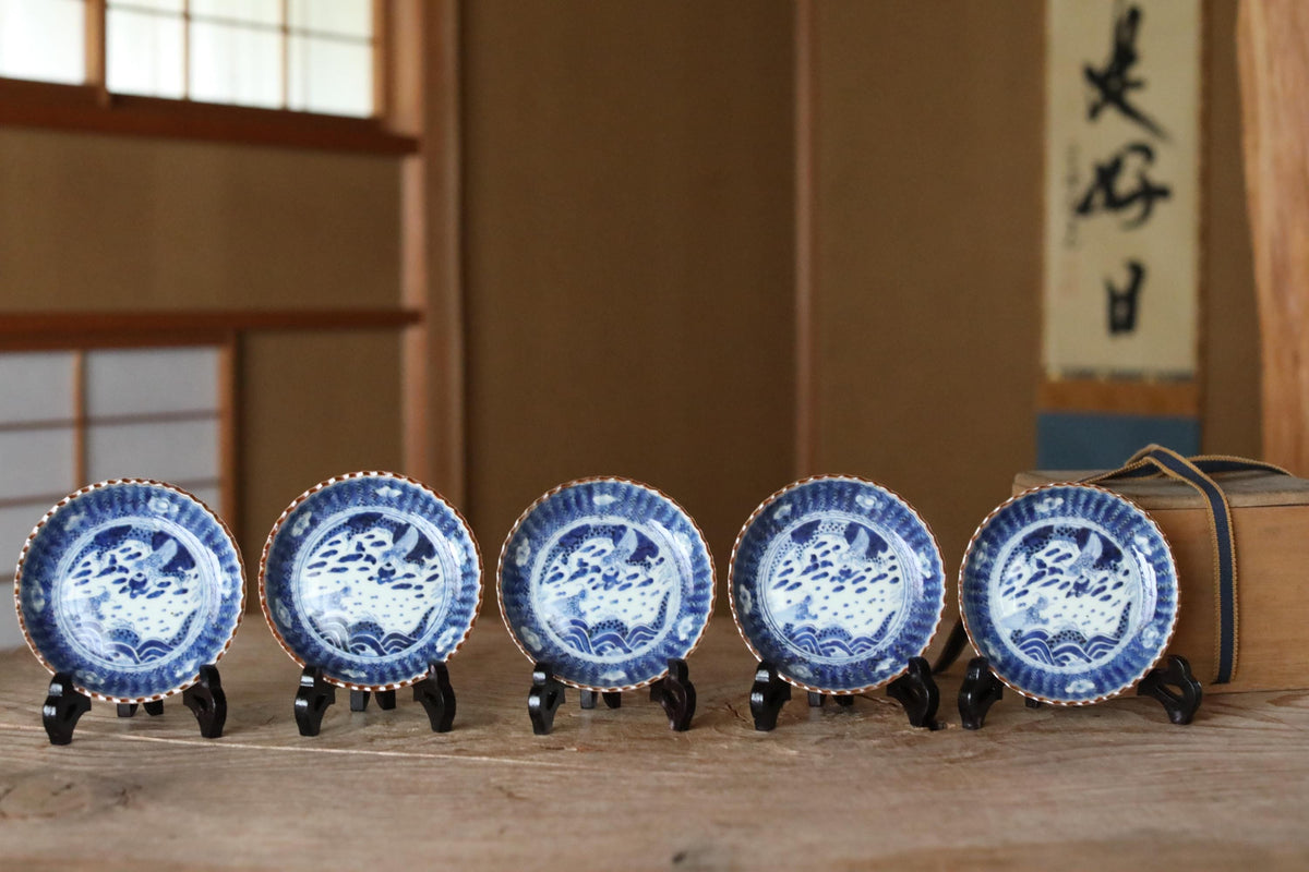 A row of five blue and white porcelain plates with intricate designs, displayed on a wooden surface.