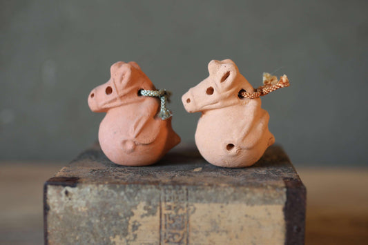 Two clay figurines of pigs sitting on a wooden surface.