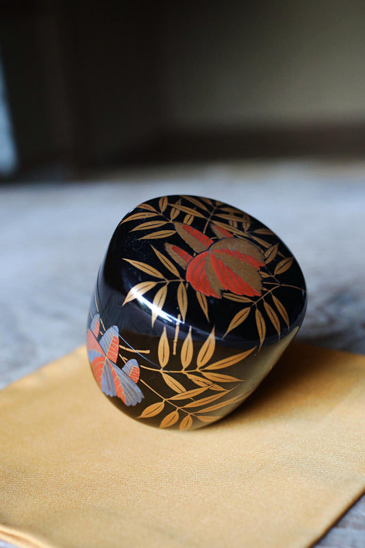 A decorative black and gold box with a floral pattern sits on a yellow cloth.