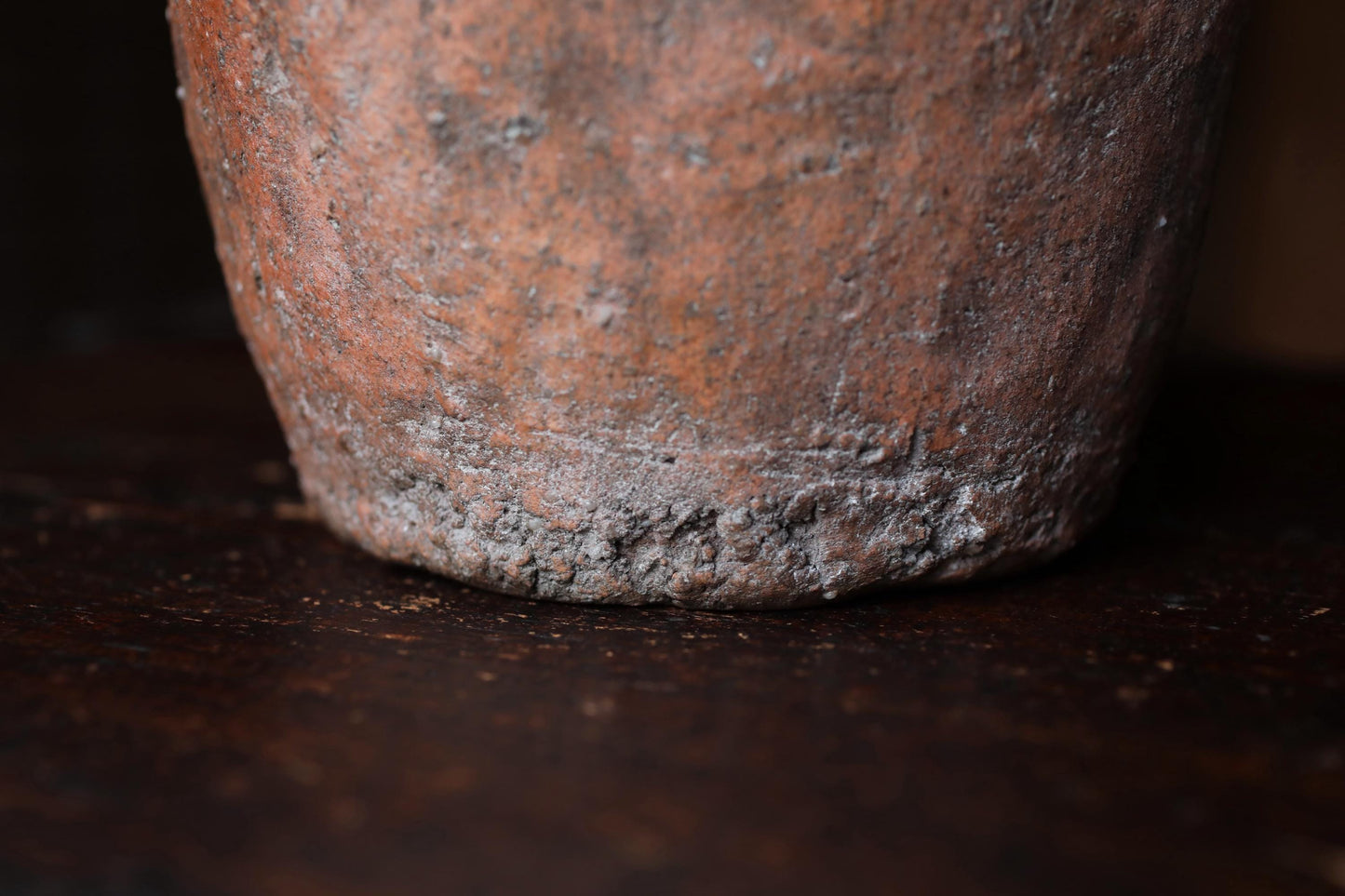 A close-up view of a weathered, textured surface, possibly a piece of pottery or a stone, with a dark background.