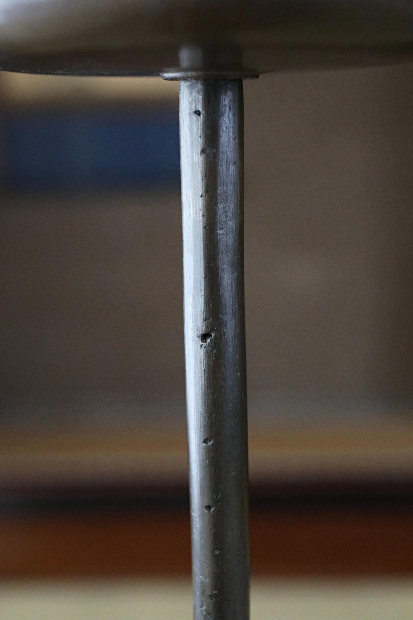 a close-up view of a metal pole or column, with a blurred background that appears to be a wooden surface.