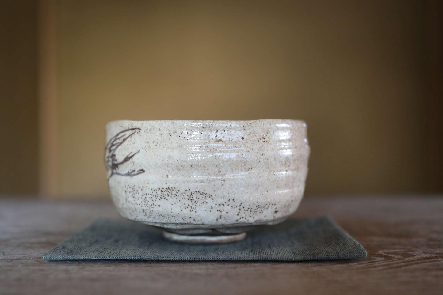 A white ceramic bowl with a black design on it, placed on a gray cloth on a wooden surface.