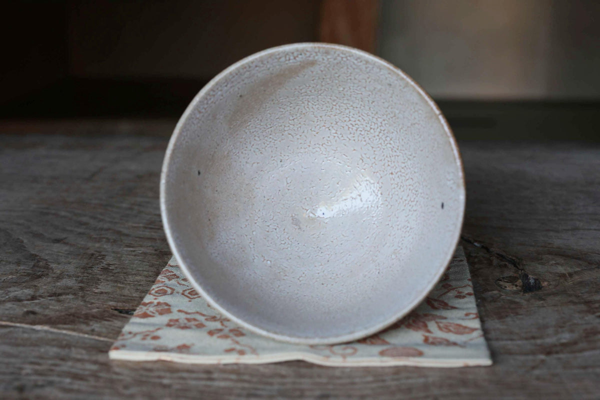 A white ceramic bowl rests on a wooden surface, with a floral patterned cloth underneath.