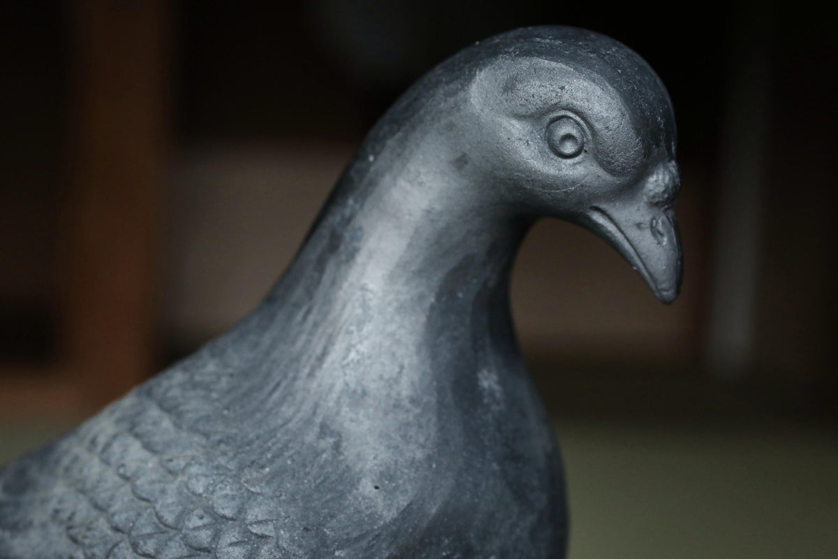 A close-up view of a black metal bird statue, possibly a pigeon, with a focused expression.