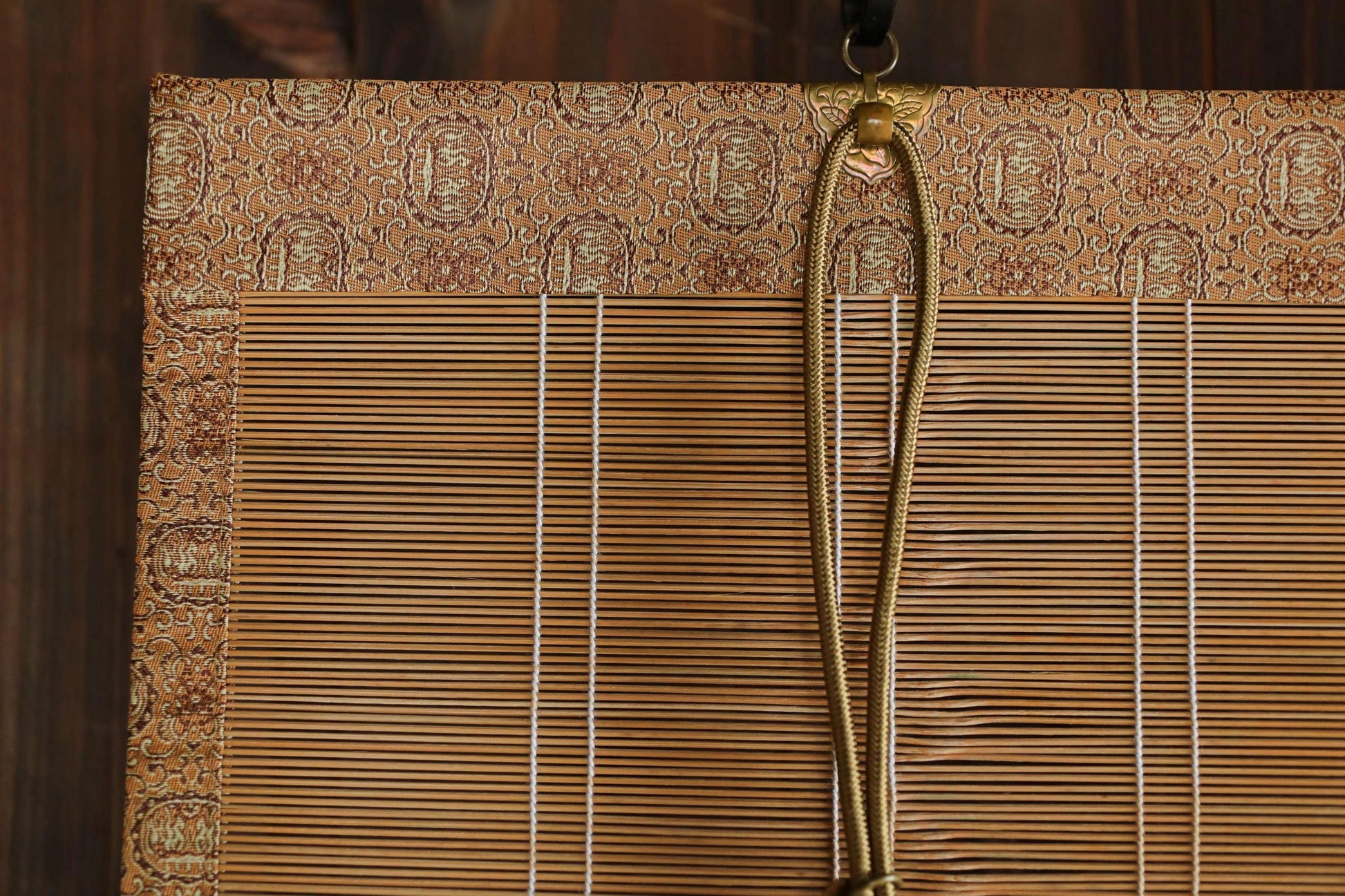 a close-up view of a bamboo blind with a gold rope hanging from it.