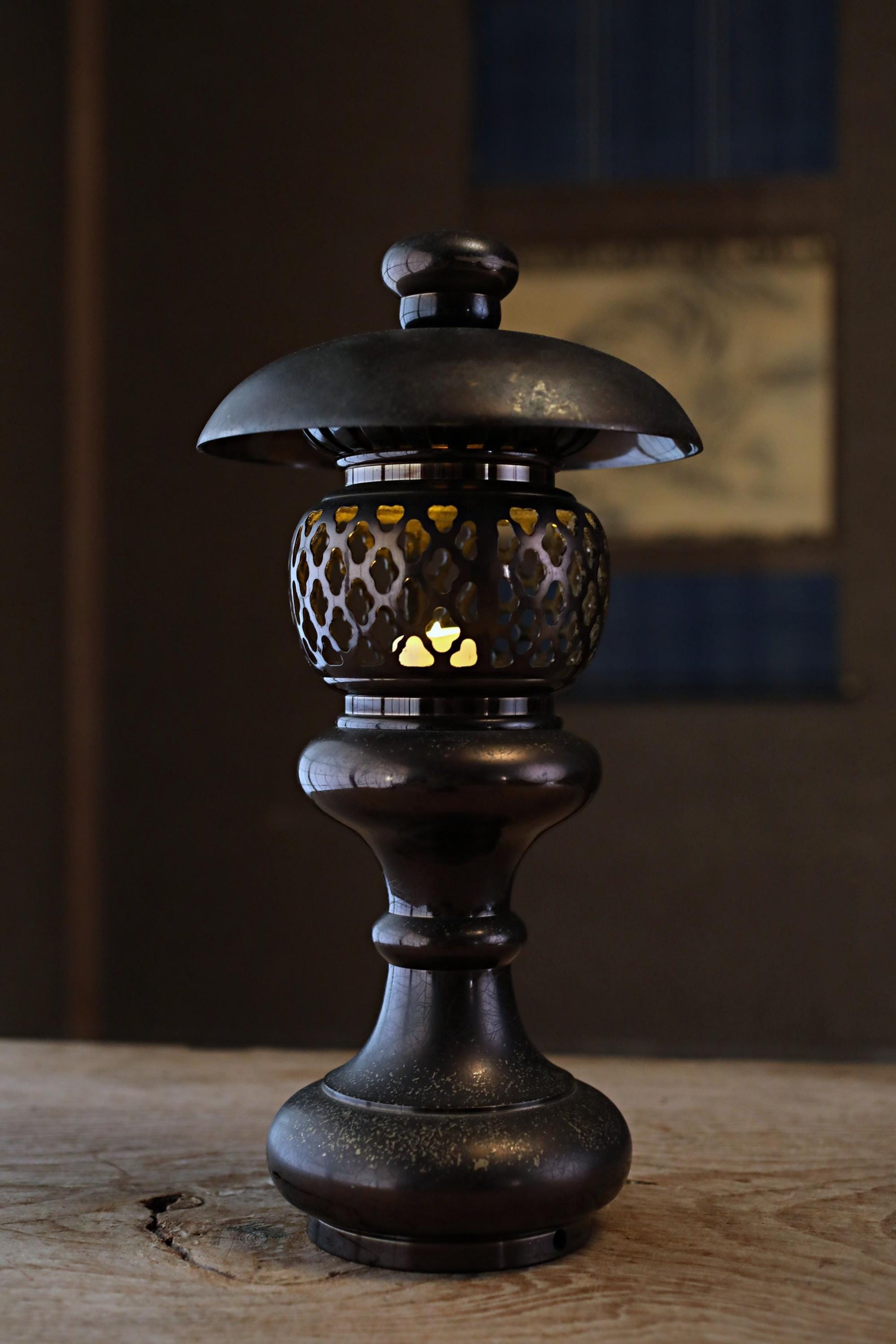 A black metal lantern with a glass shade is lit, casting a warm glow on a wooden surface.