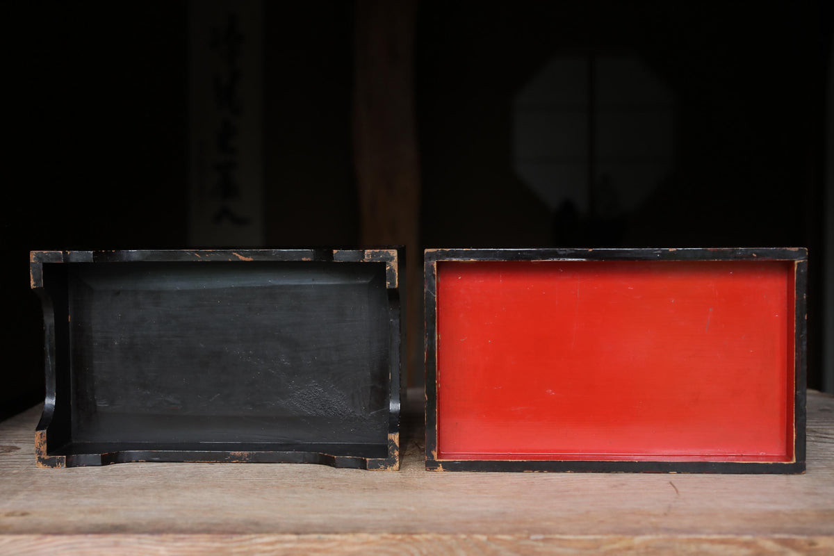 two wooden boxes, one black and one red, placed side by side on a wooden surface.