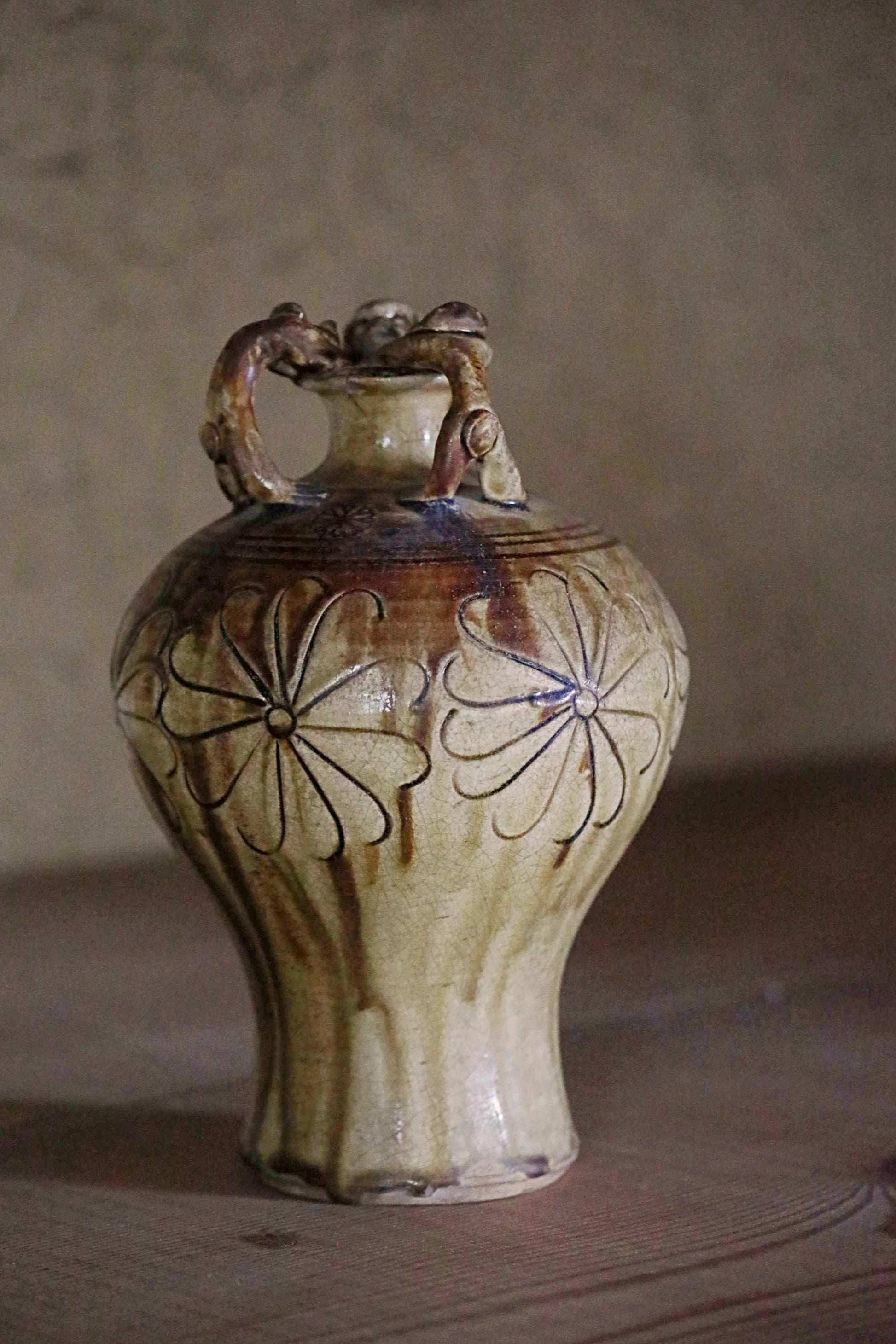 A ceramic vase with a floral design on its surface, sitting on a wooden surface against a plain background.