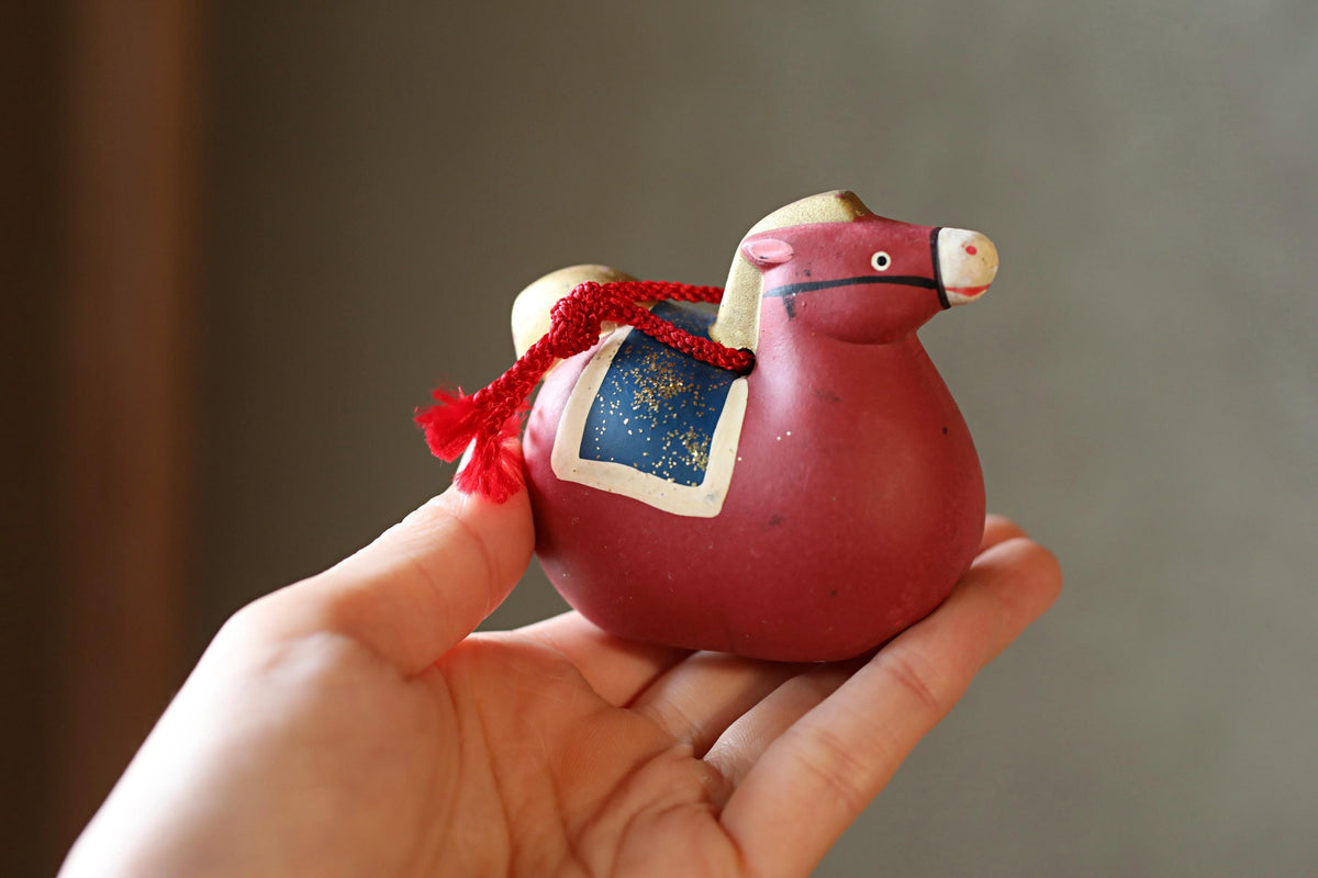 A hand holding a small red and blue ceramic horse figurine.