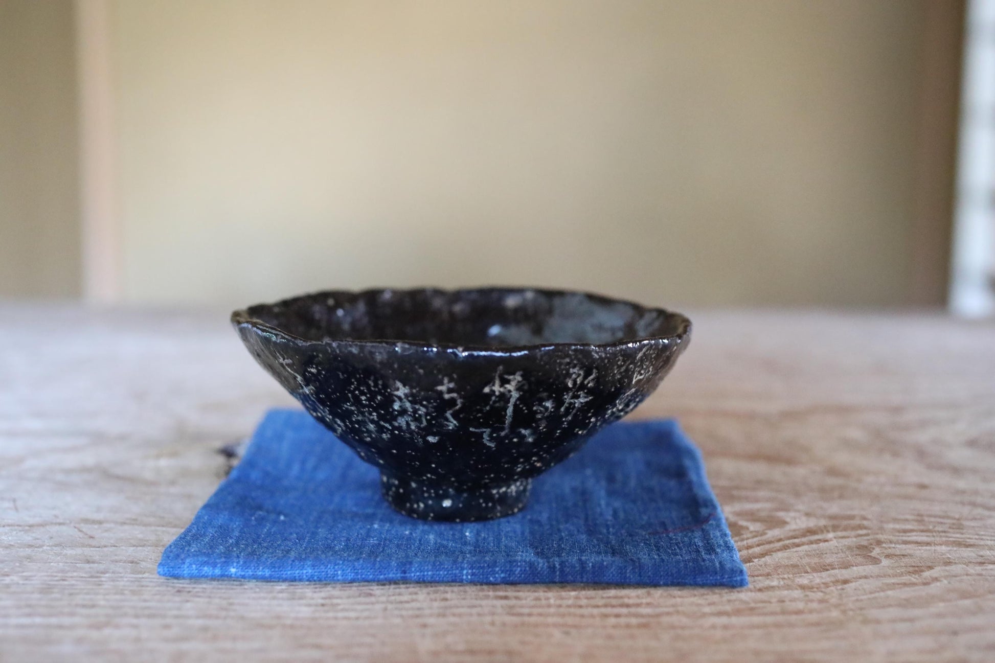 A black ceramic bowl with a speckled pattern sits on a blue cloth on a wooden surface.