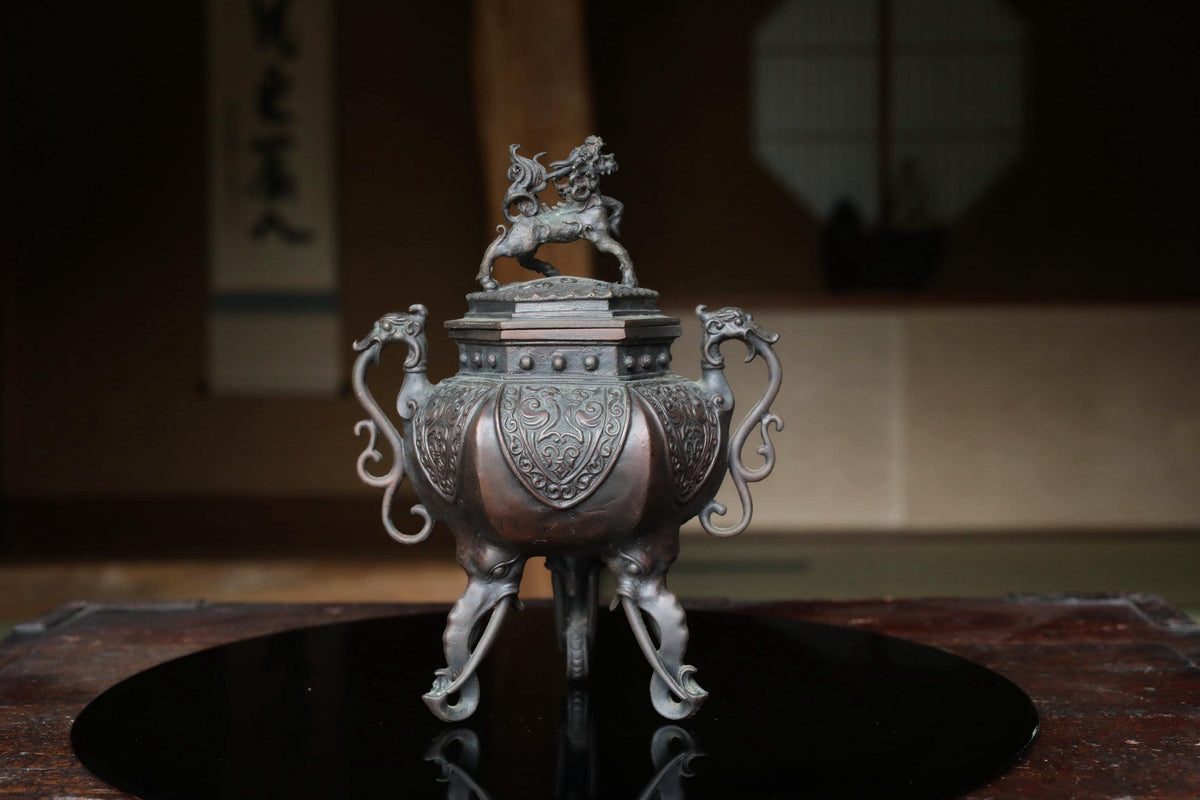 A decorative metal incense burner with a dragon figure on top, placed on a black circular surface.