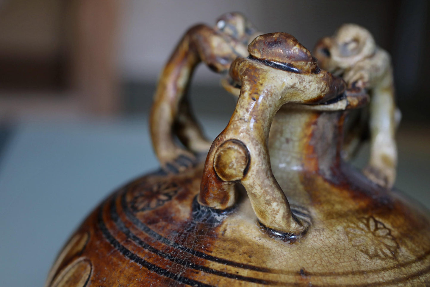 A close-up image of a ceramic vase with intricate designs and patterns, featuring two handles and a dragon-like figure on the top.