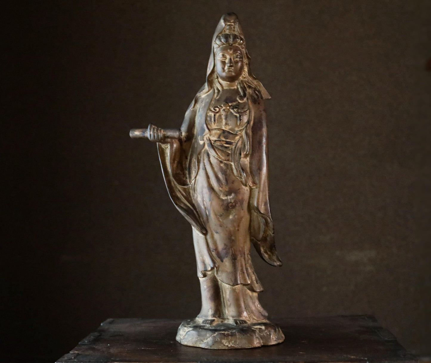 A bronze statue of a female deity, likely a goddess, standing on a pedestal and holding a staff.