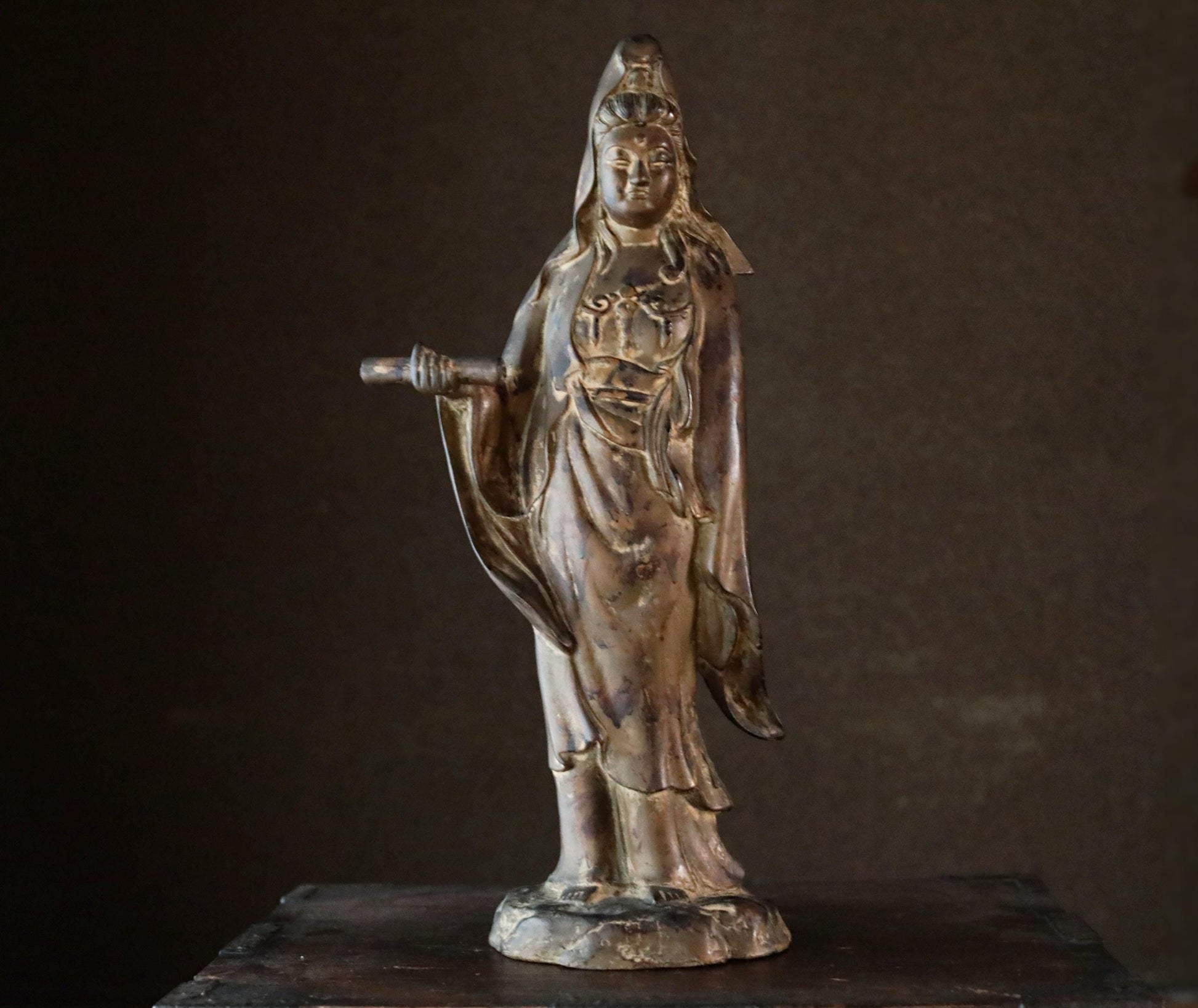 A bronze statue of a female deity, likely a goddess, standing on a pedestal and holding a staff.