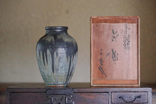 a ceramic vase with a blue and white speckled design, placed on a wooden surface next to a wooden box with Japanese characters.
