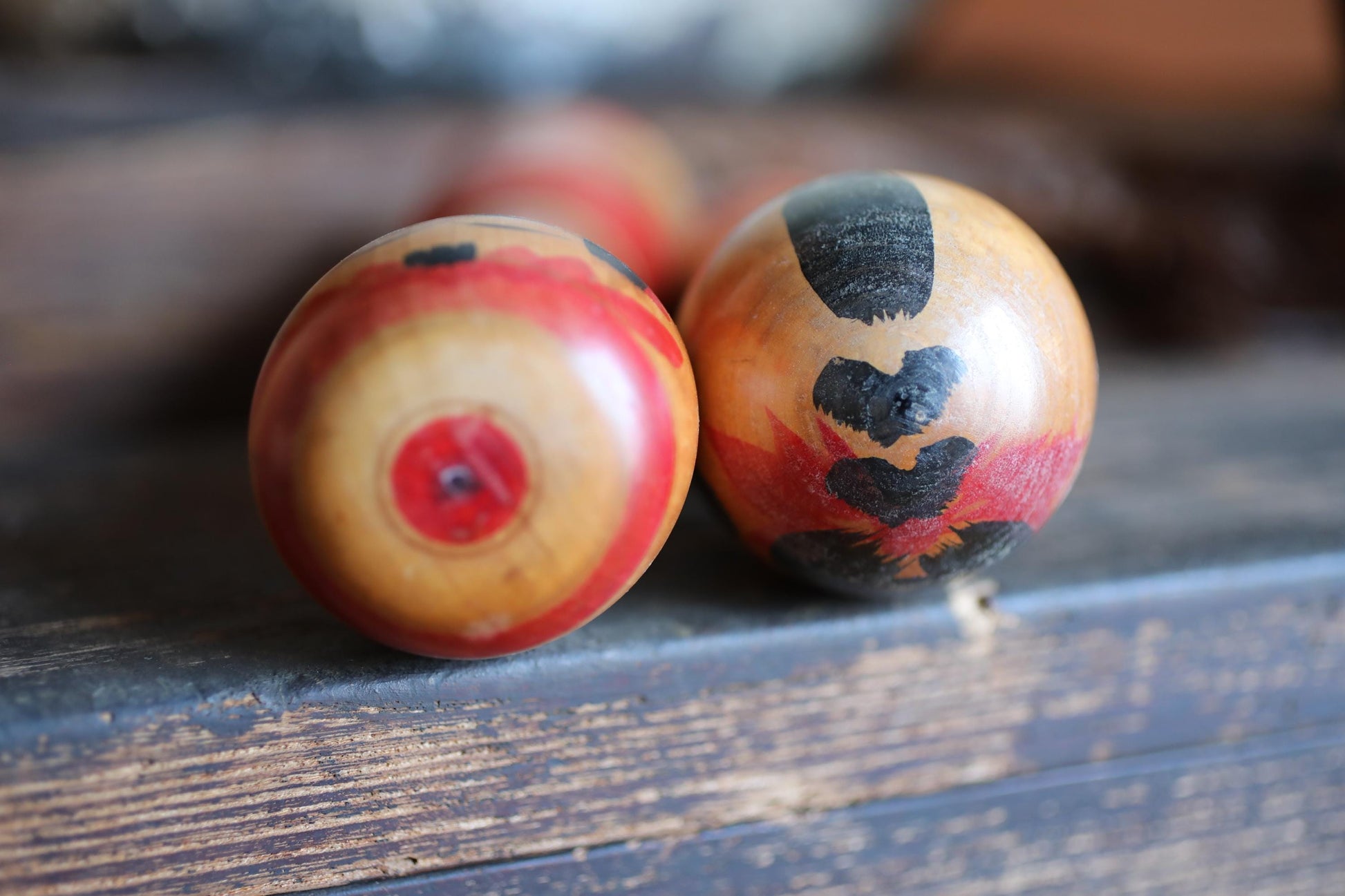 two colorful wooden objects with black and red designs on them, placed on a wooden surface.