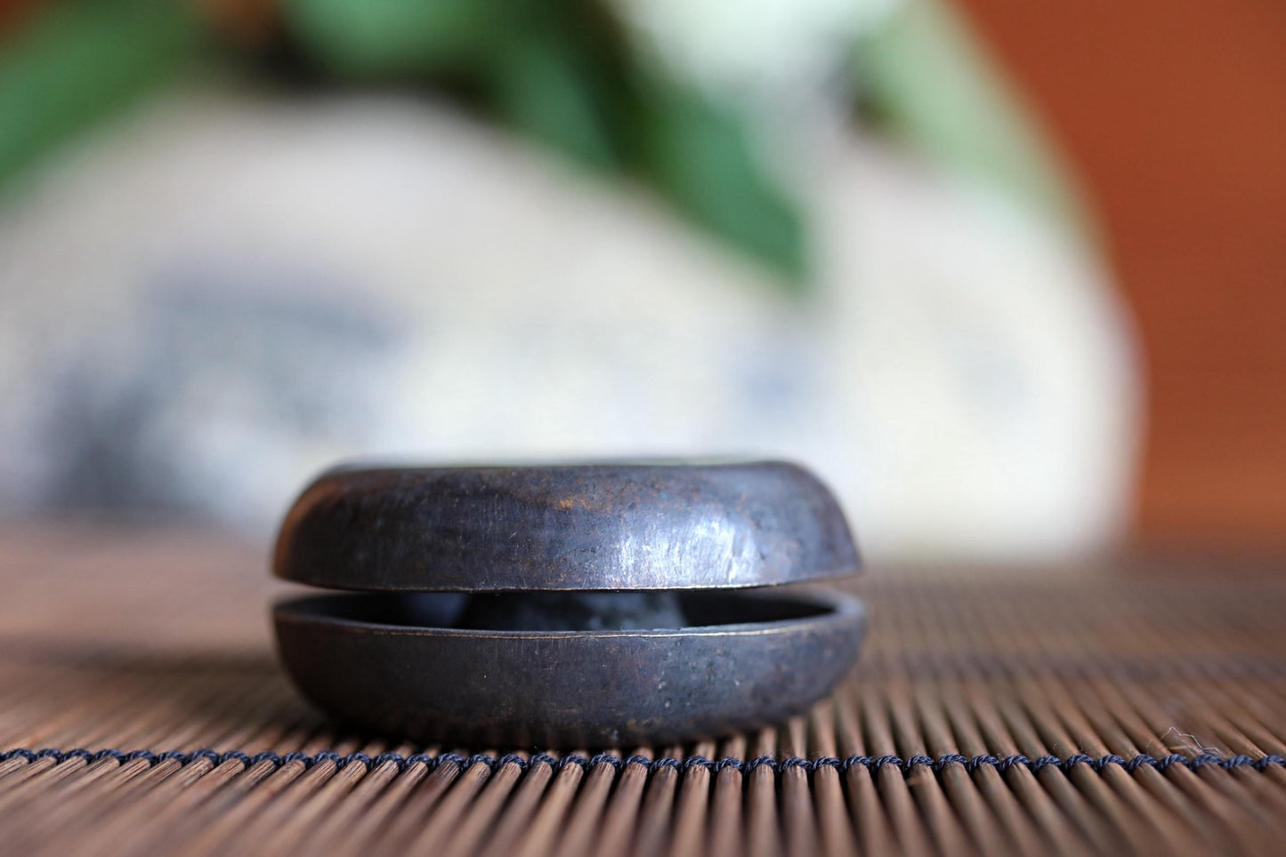 A black metal object, possibly a bowl or container, is placed on a bamboo mat in the foreground of the image.