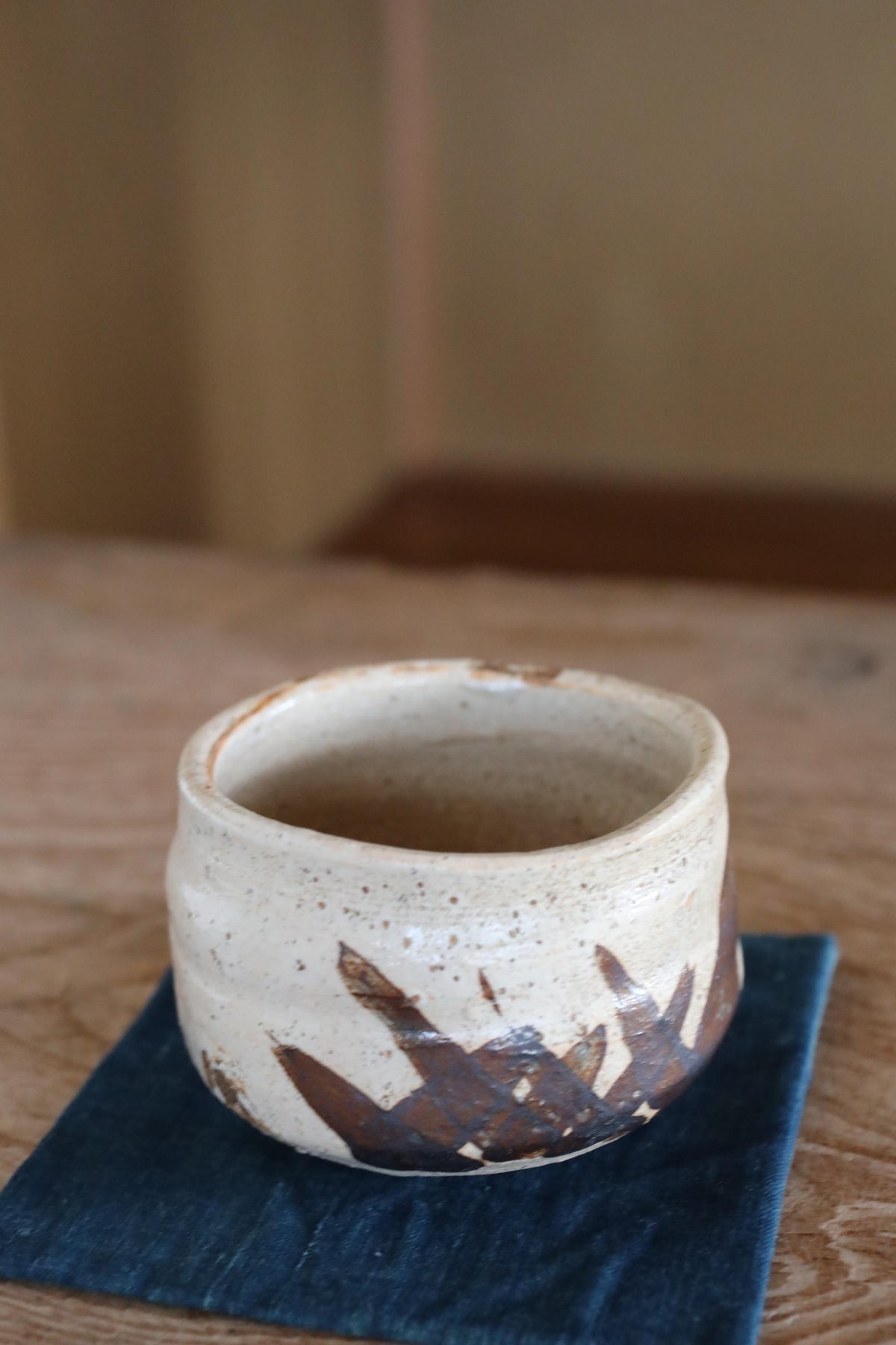 A white ceramic mug with brown designs sits on a blue cloth on a wooden table.
