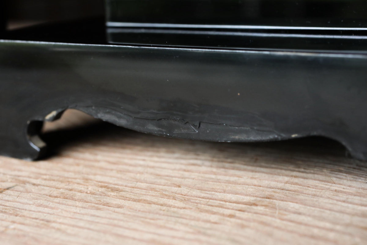 A close-up view of a black metal object, possibly a piece of furniture or a tool, resting on a wooden surface.