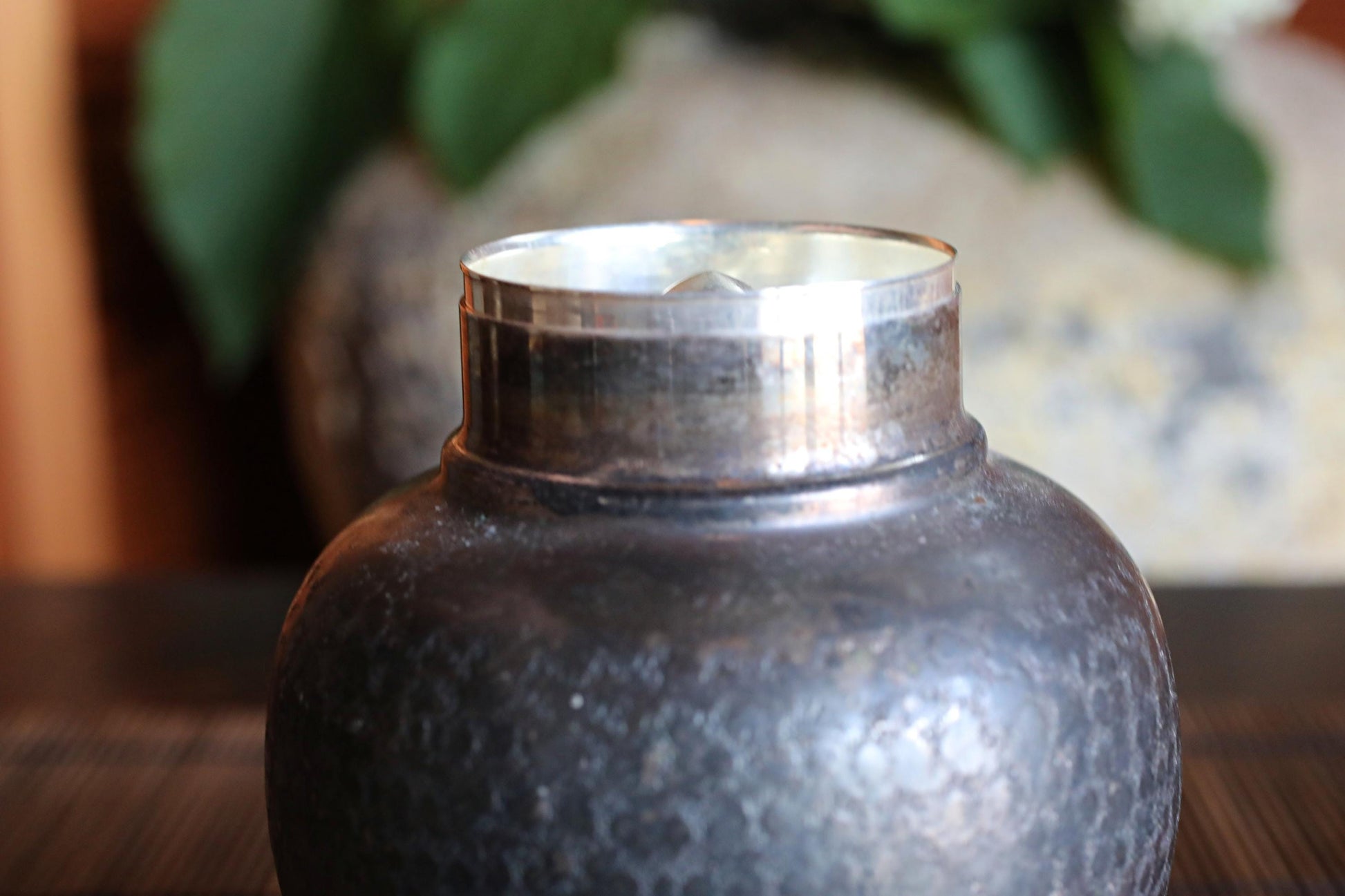 A close-up view of a metal vase or container with a metallic sheen, placed on a wooden surface.