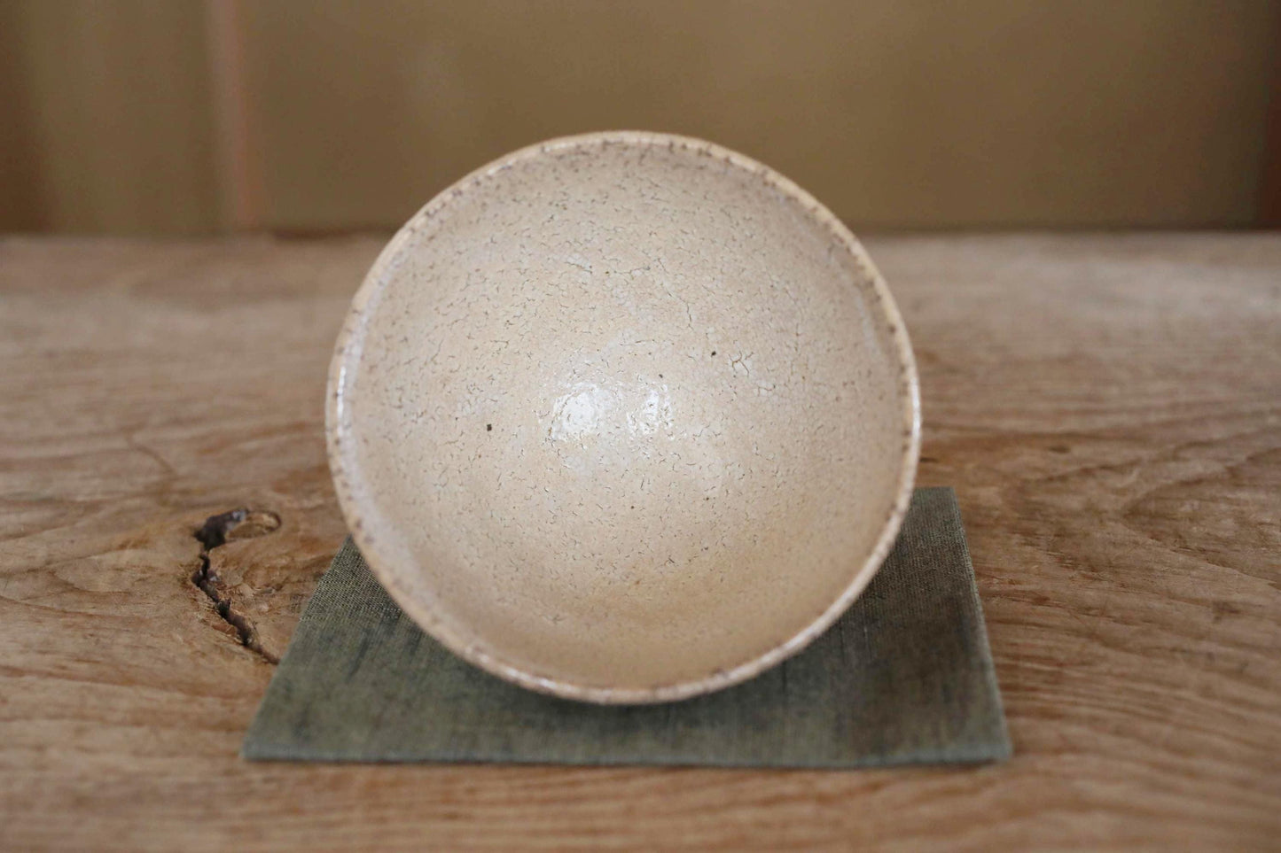 A white ceramic bowl with a speckled texture sits on a green coaster on a wooden surface.