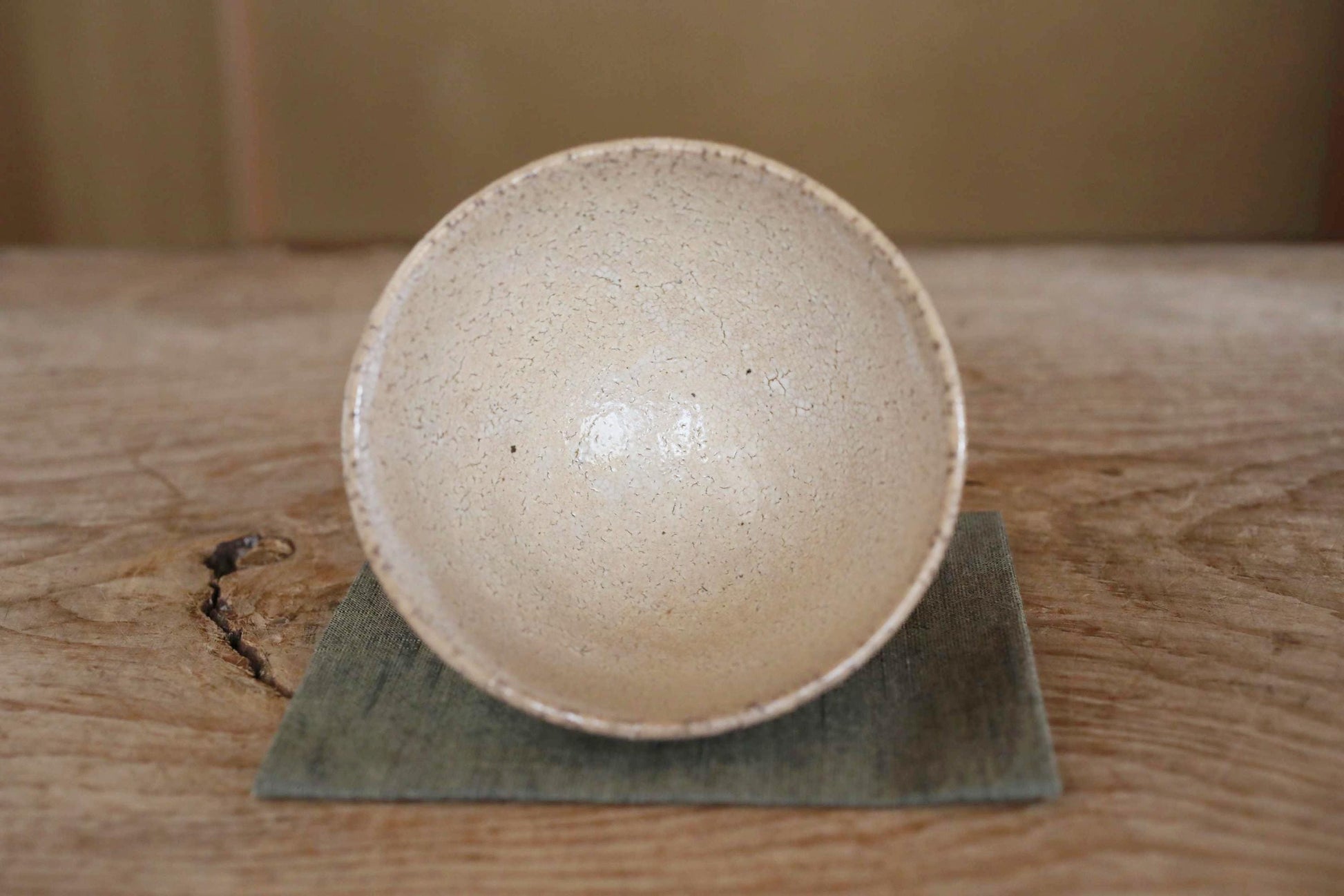 A white ceramic bowl with a speckled texture sits on a green coaster on a wooden surface.