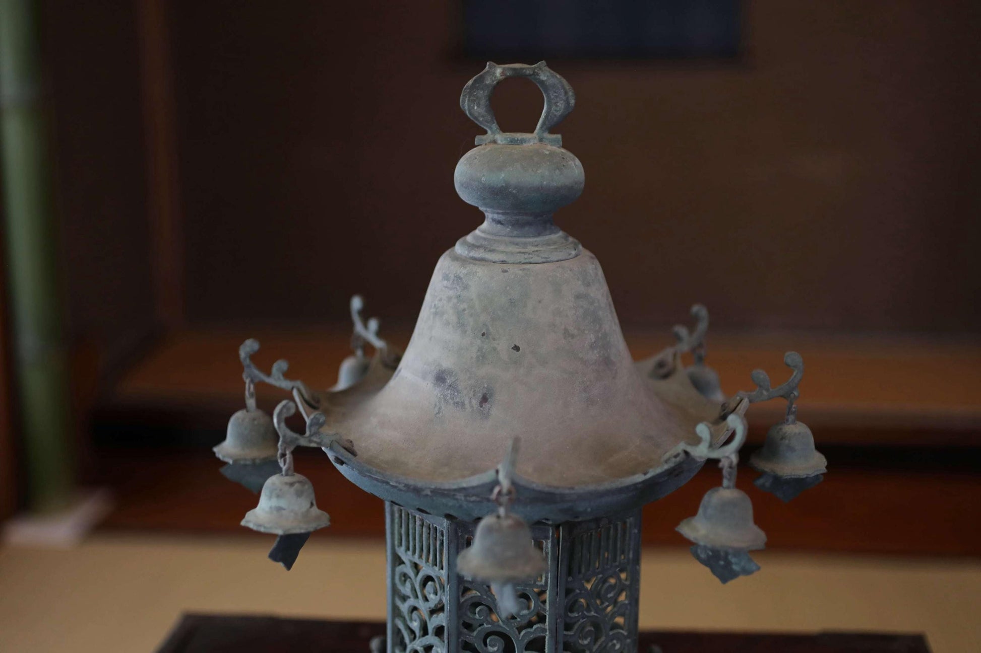 An antique metal lantern with a decorative top and hanging bells, displayed on a wooden surface.