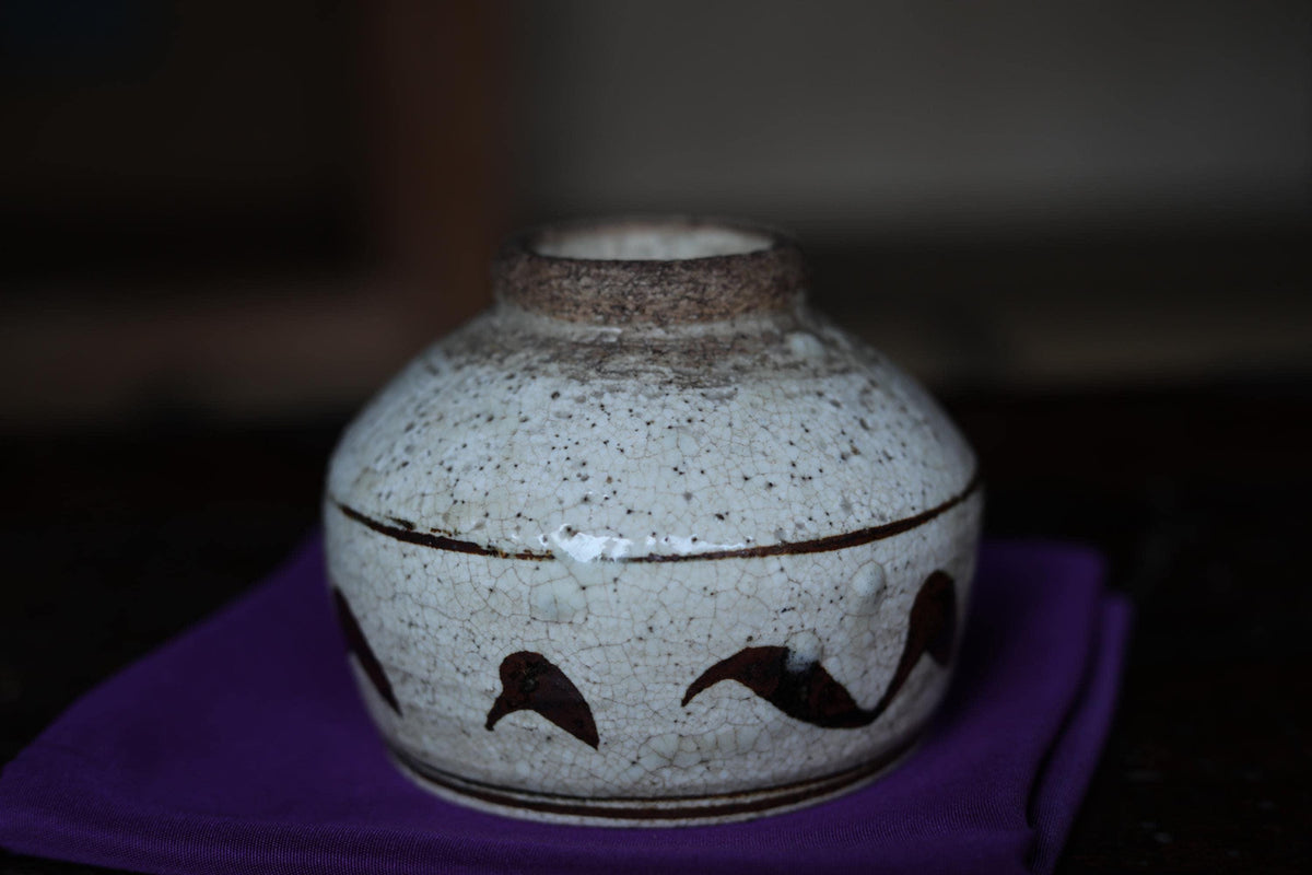 A white ceramic vase with a black design on it, placed on a purple cloth.