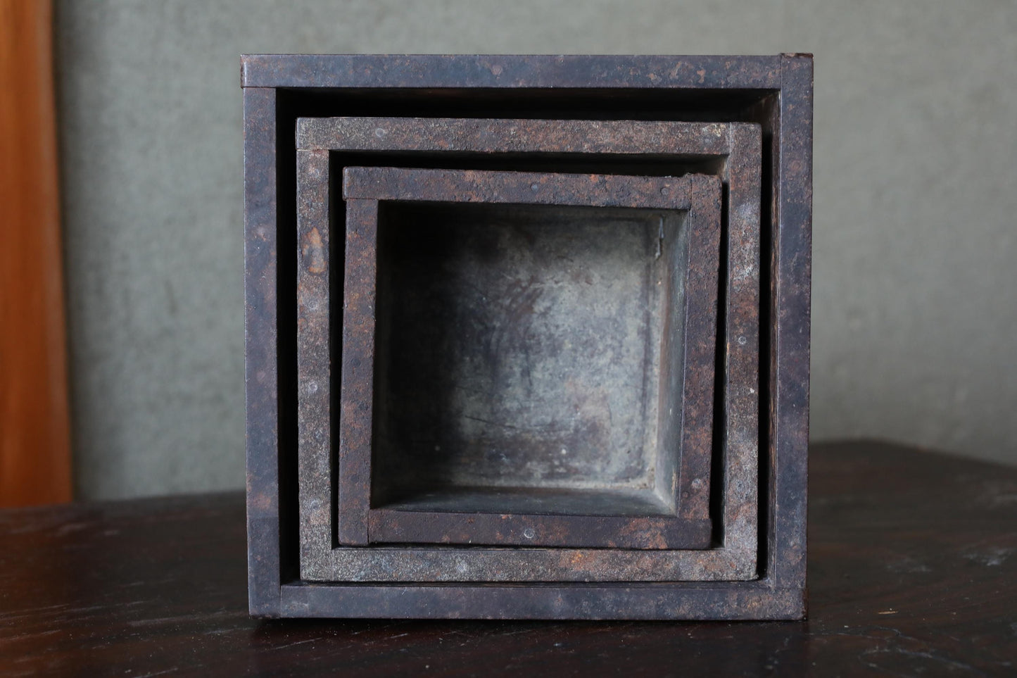 A set of three rusted metal containers stacked on top of each other, with a wooden surface in the background.