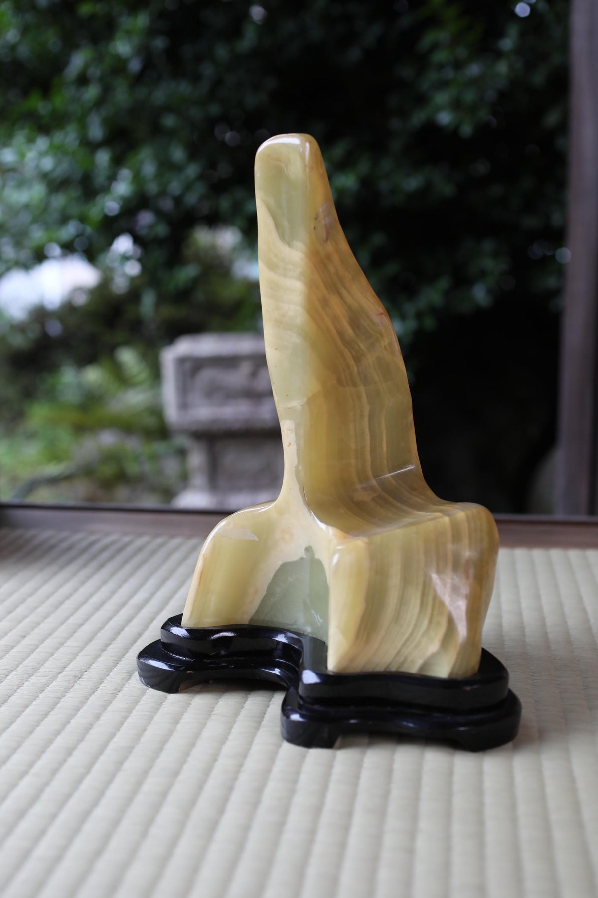 a sculpture of a yellowish-brown, abstract shape sitting on a black base, placed on a beige surface.