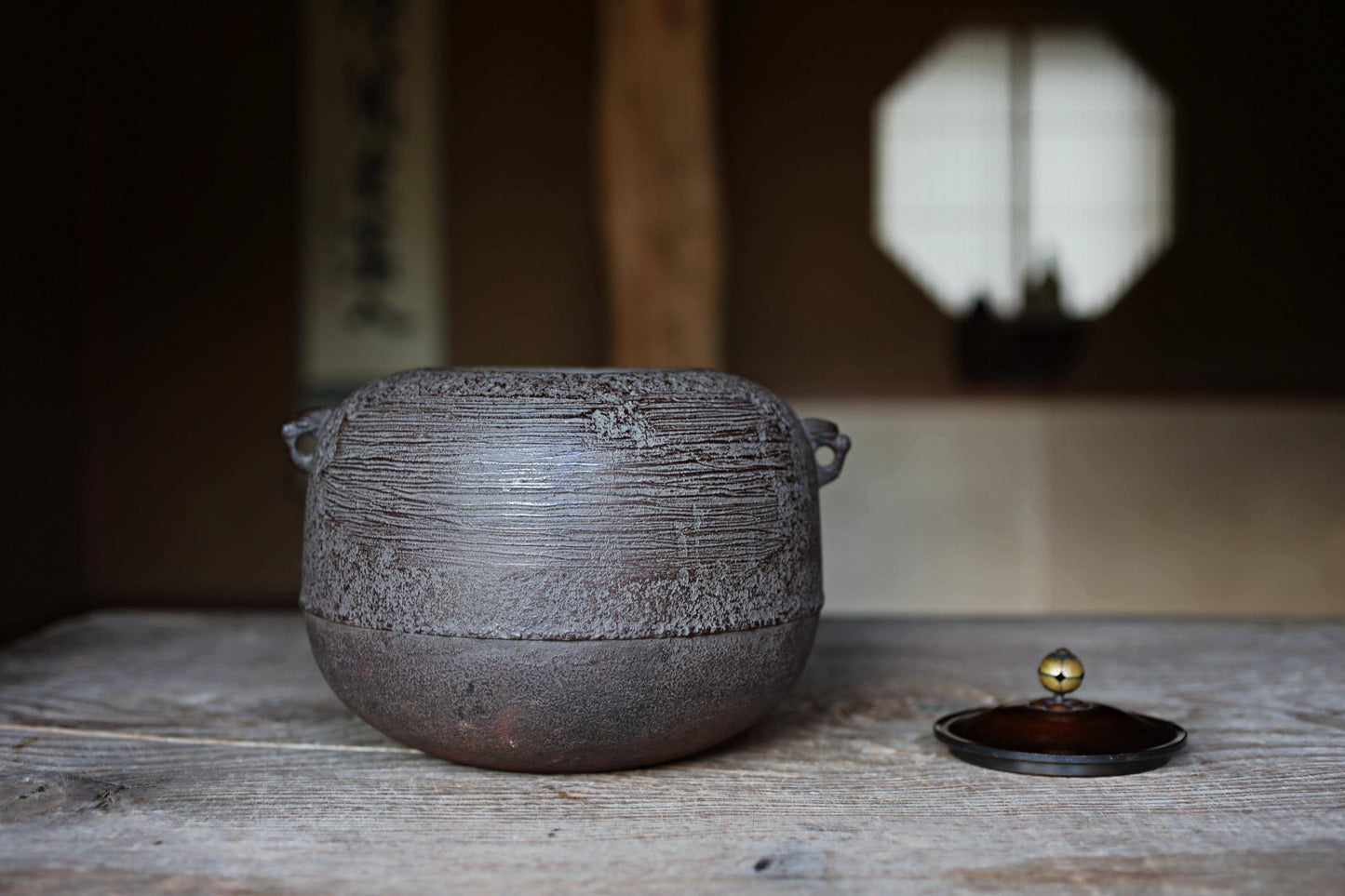 A large, round, black pot with a handle sits on a wooden surface, with a small, round lid placed next to it.