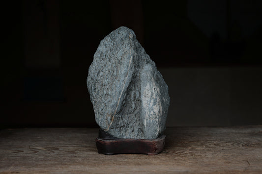 A large, gray rock sits on a wooden surface, with a dark background.