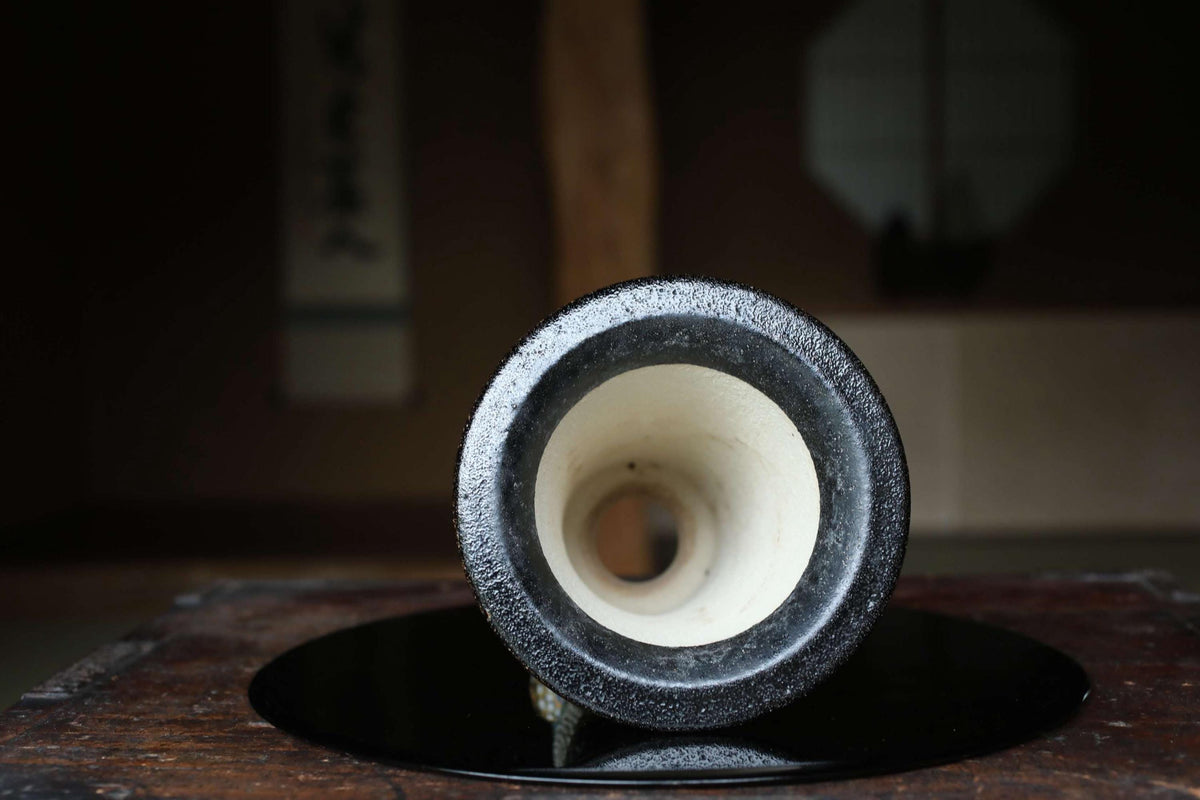 A black and white ceramic object with a white interior is placed on a wooden surface, with a blurred background.