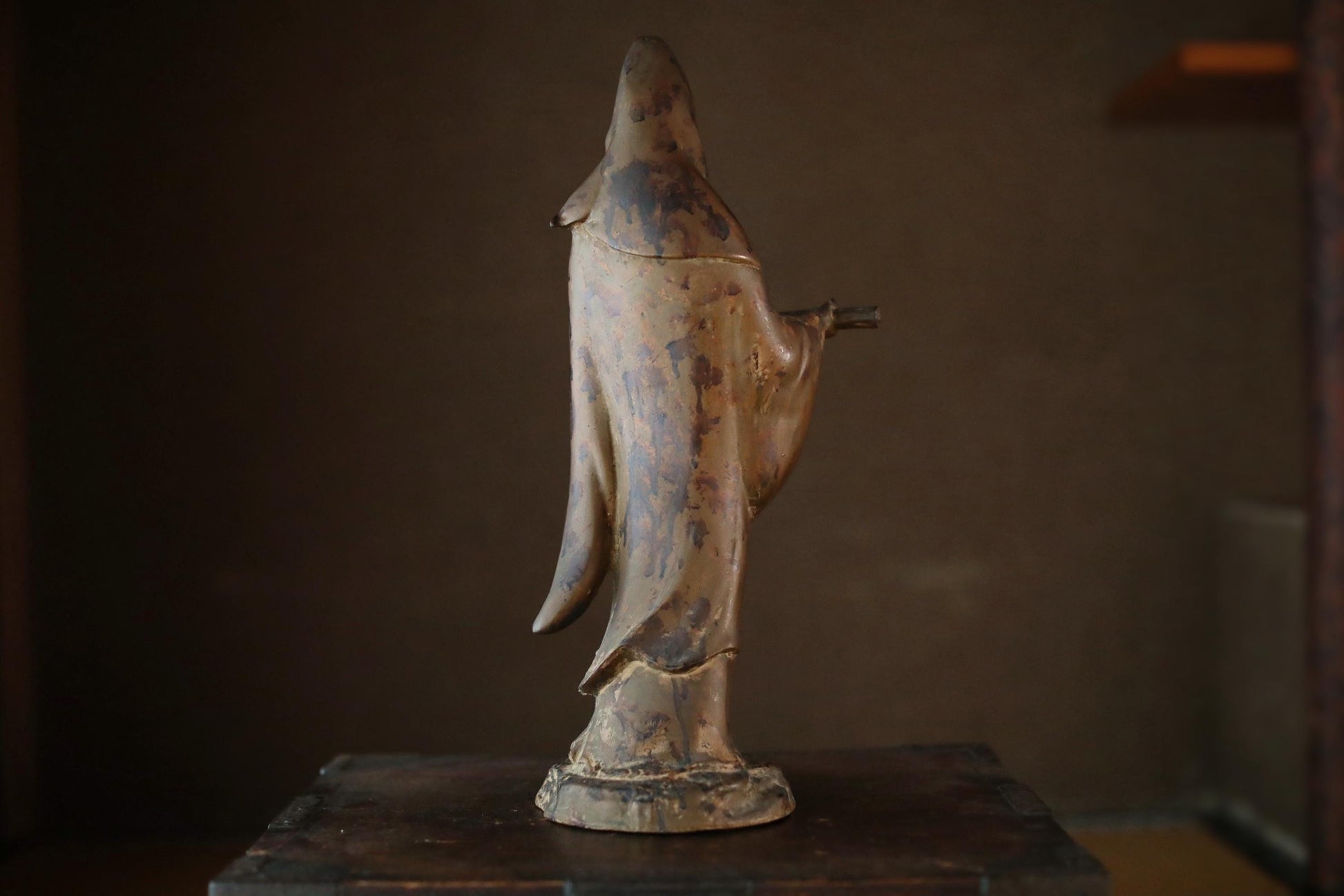 An old, weathered statue of a person, possibly a deity or religious figure, standing on a wooden surface.