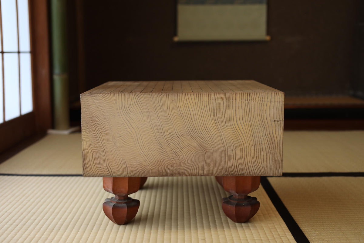 A wooden table with a natural finish sits on a tatami mat in a room with a dark background.