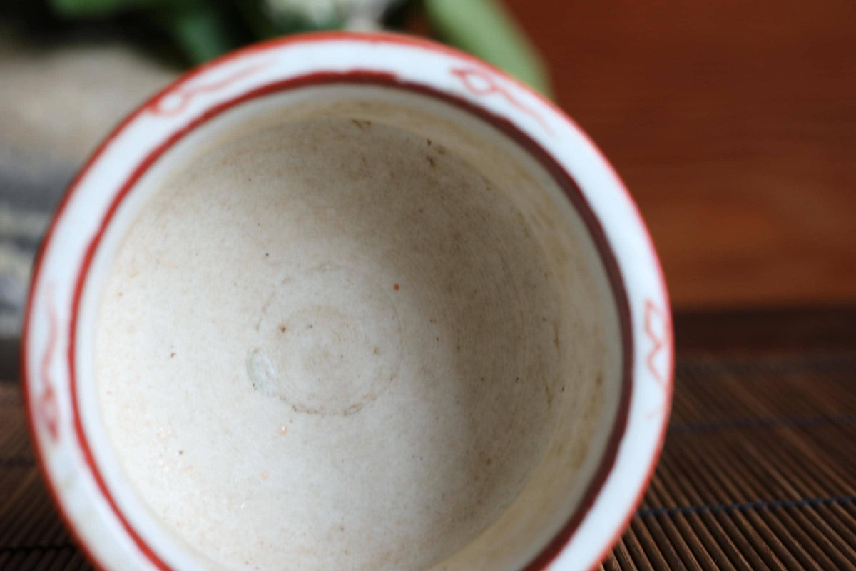 A close-up view of a white ceramic bowl with a red rim, placed on a wooden surface.