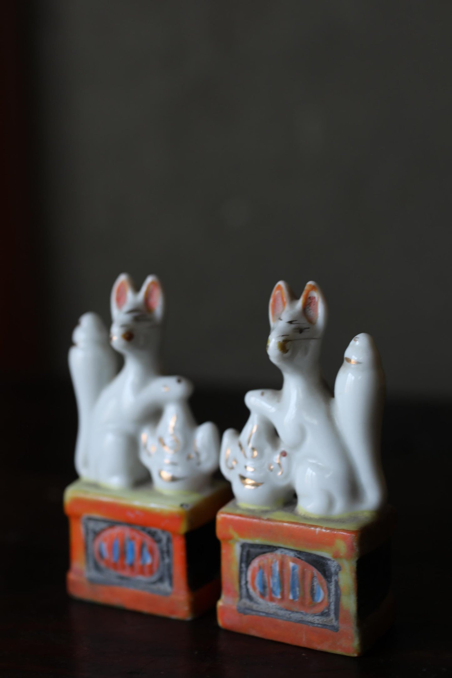 Two white ceramic figurines of cats sitting on top of a red and orange box with a decorative border.