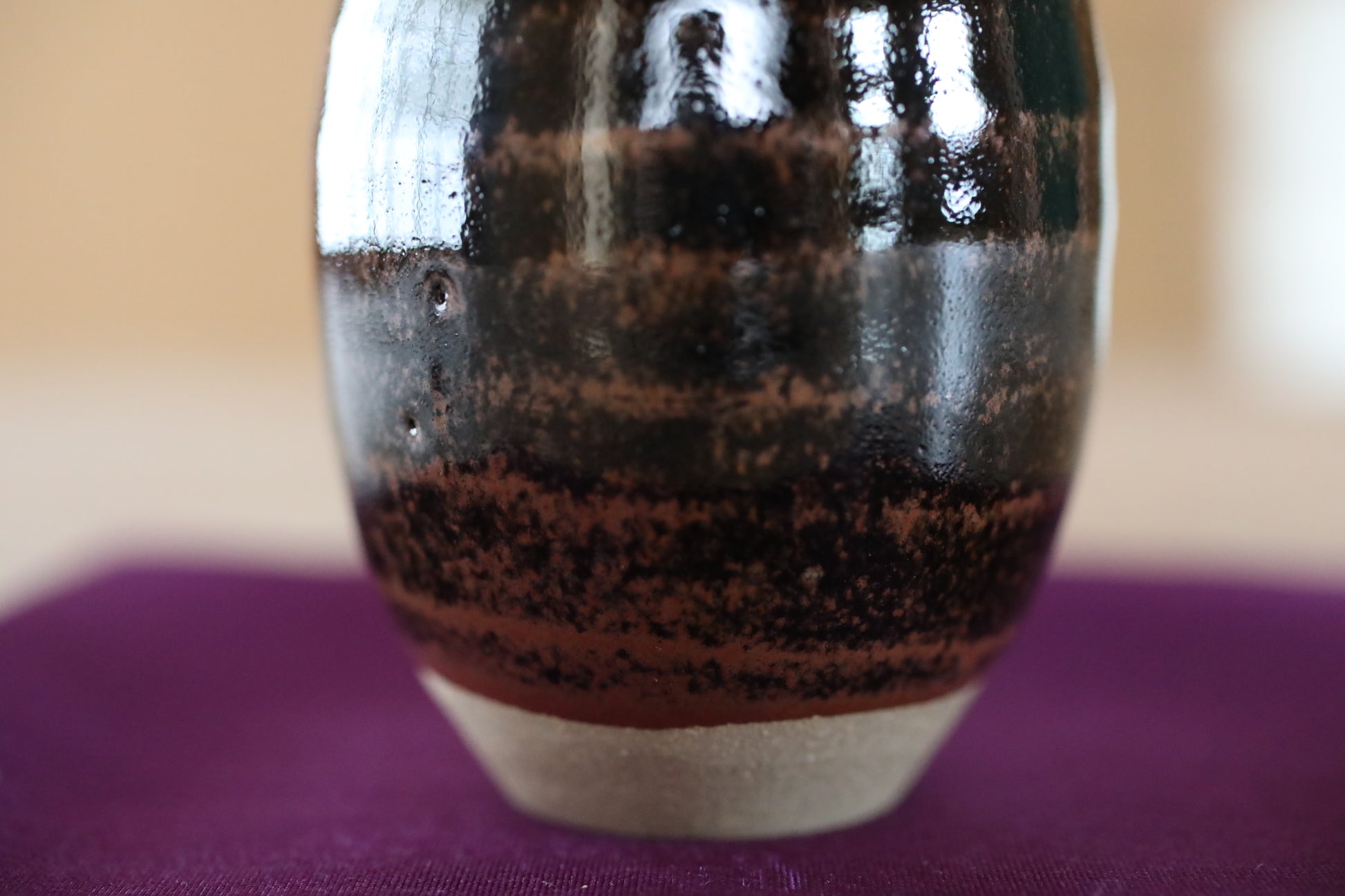A close-up view of a ceramic vase with a dark brown and black striped pattern, resting on a purple surface.
