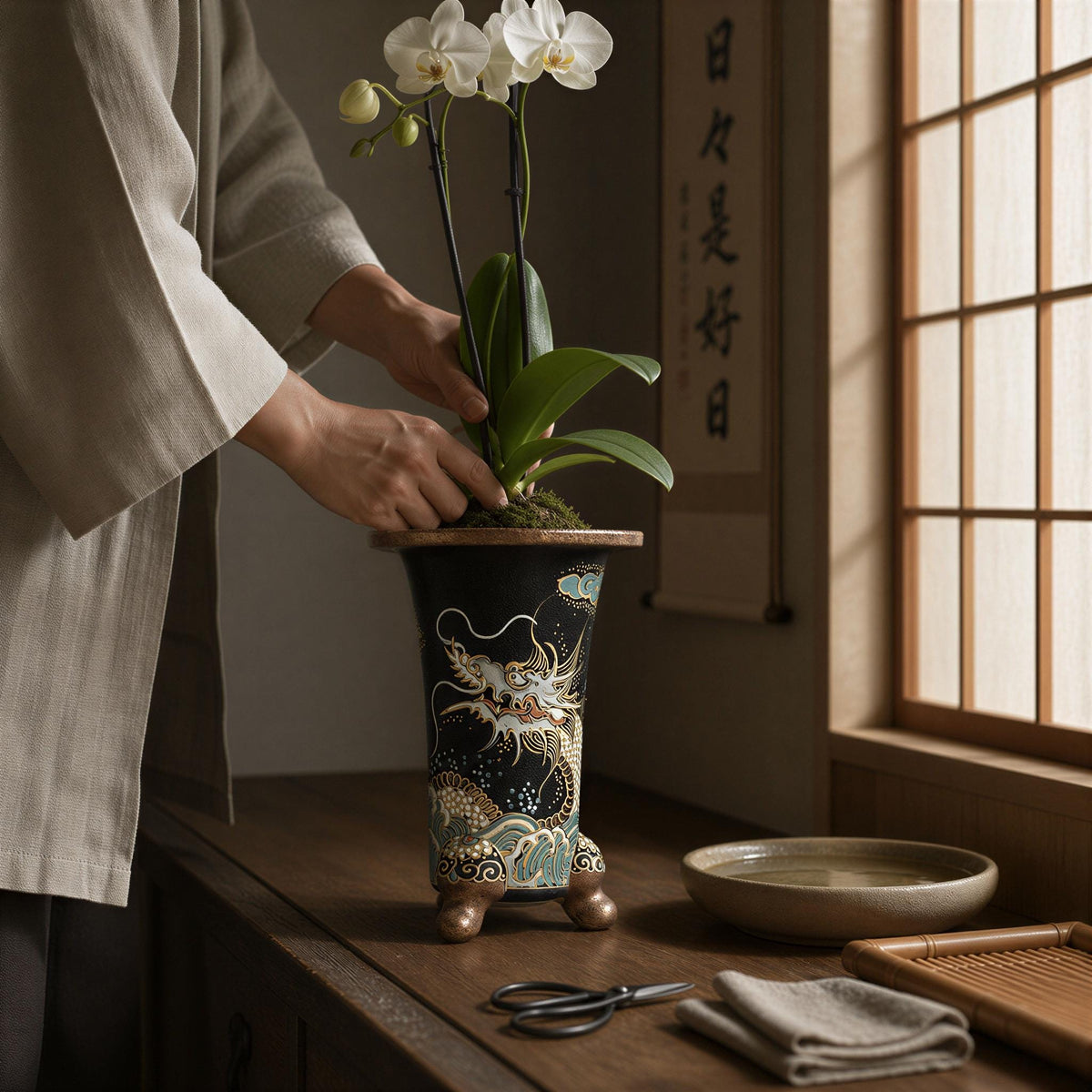 A person is carefully arranging a potted orchid plant in a decorative vase on a wooden surface.