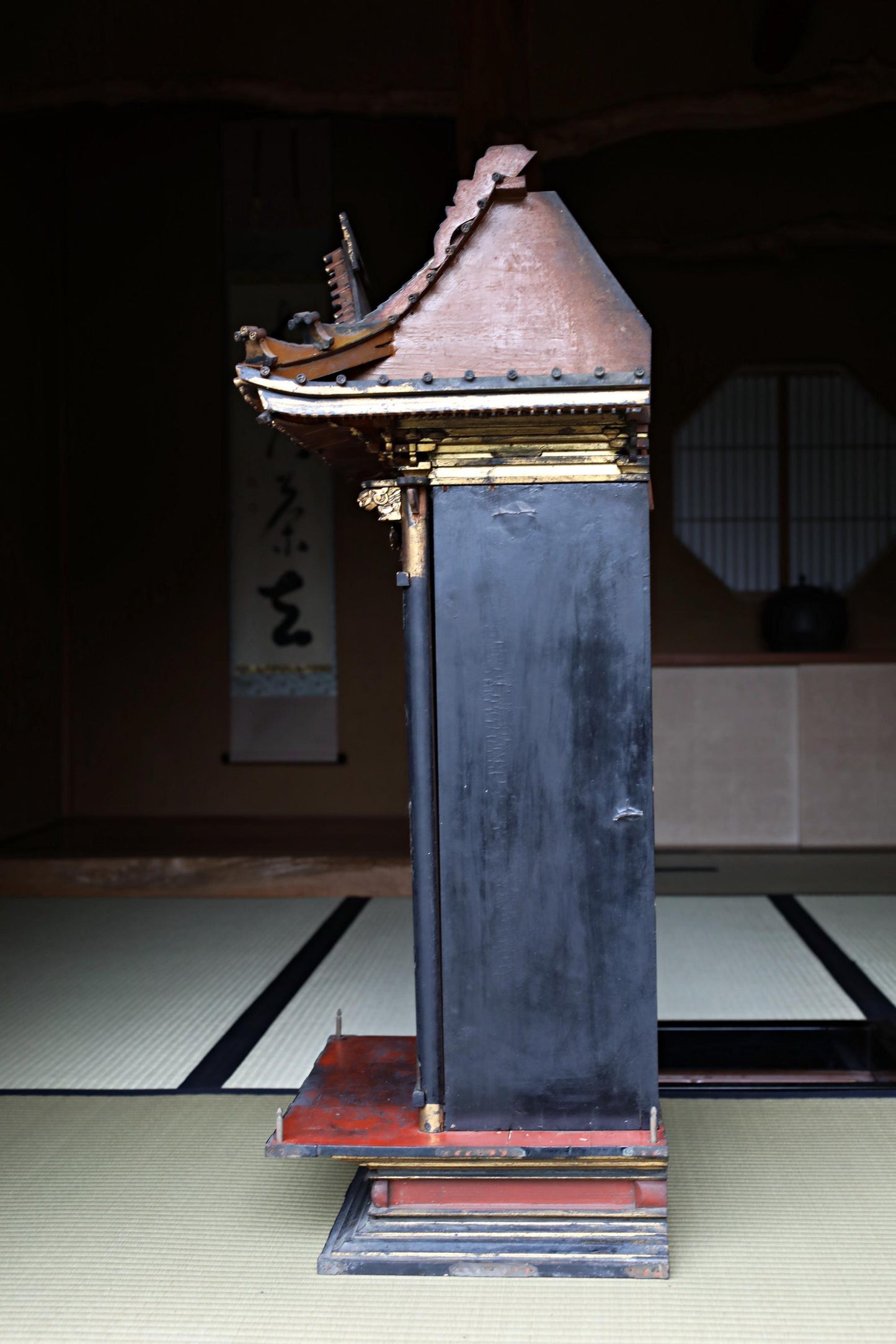 a tall, ornate, and intricately designed wooden structure with a black and red color scheme, standing on a tatami mat.