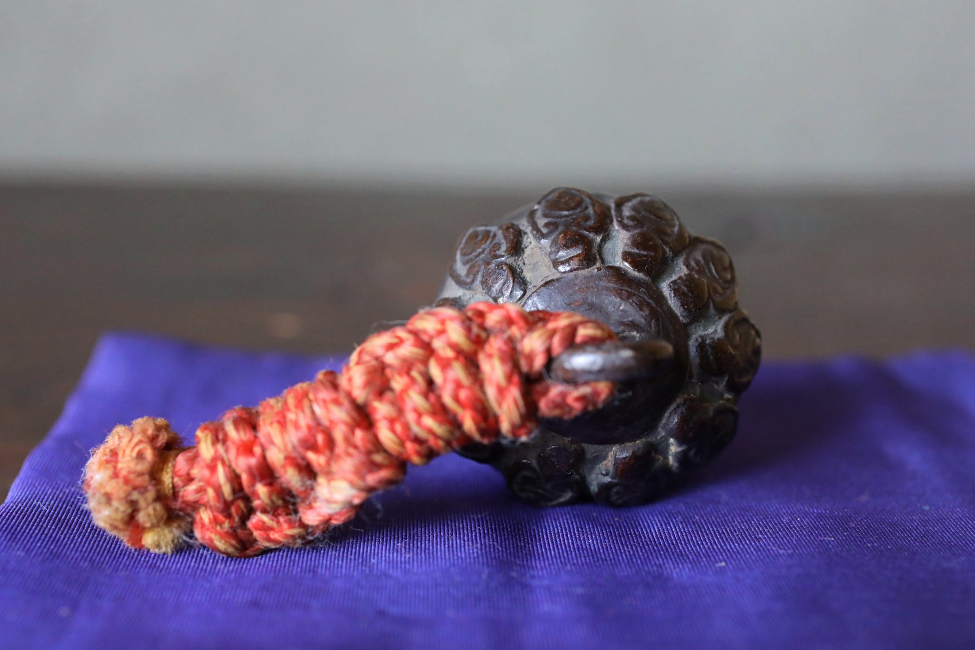A dark brown, intricately carved object with a red and yellow rope wrapped around it, resting on a blue cloth.