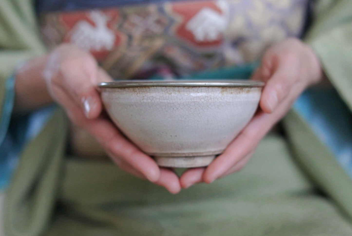 A person's hands holding a white ceramic bowl with a green patterned cloth visible behind them.