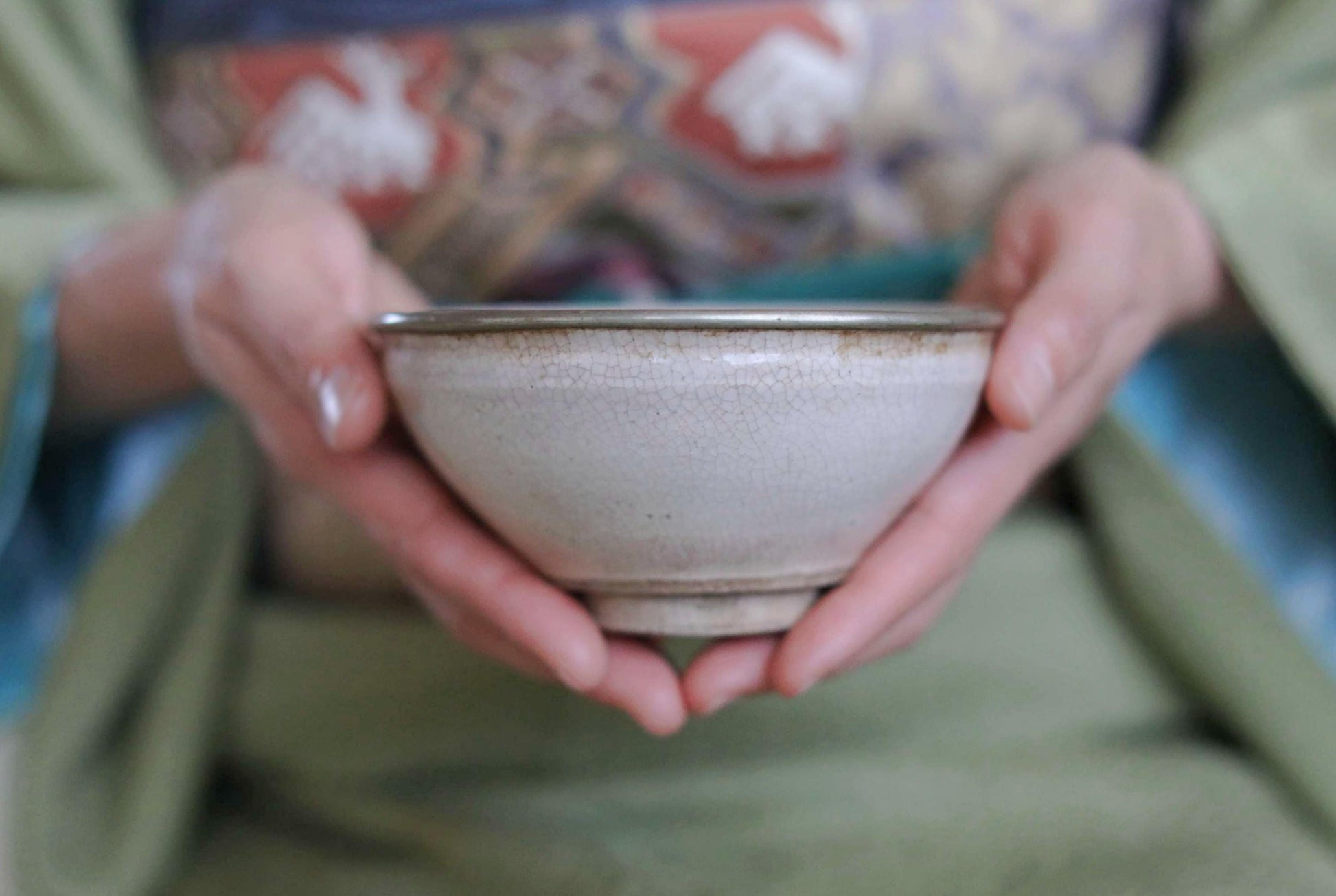 A person's hands holding a white ceramic bowl with a green patterned cloth visible behind them.