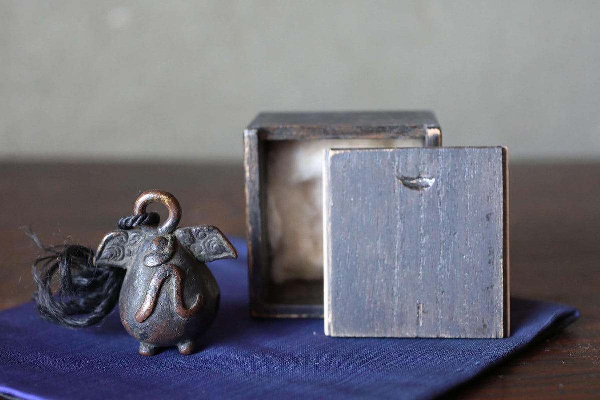 a small metal bell with a wooden box lid, placed on a blue cloth.