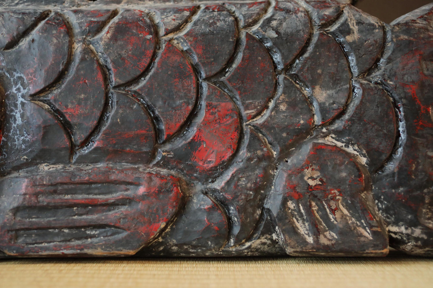a close-up view of a carved wooden surface with a pattern of red and black colors. The surface appears to be weathered and aged, with visible cracks and crevices. The image does not contain any text or other discernible objects or scenes.