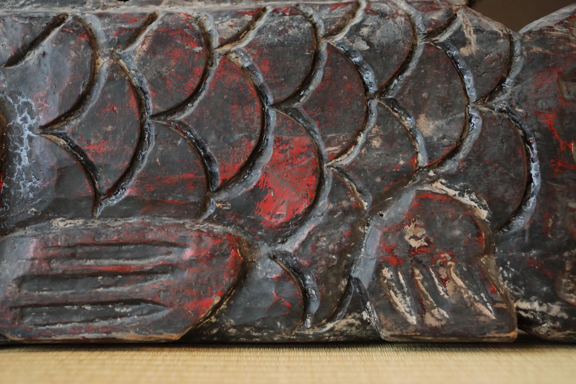 a close-up view of a carved wooden surface with a pattern of red and black colors. The surface appears to be weathered and aged, with visible cracks and crevices. The image does not contain any text or other discernible objects or scenes.