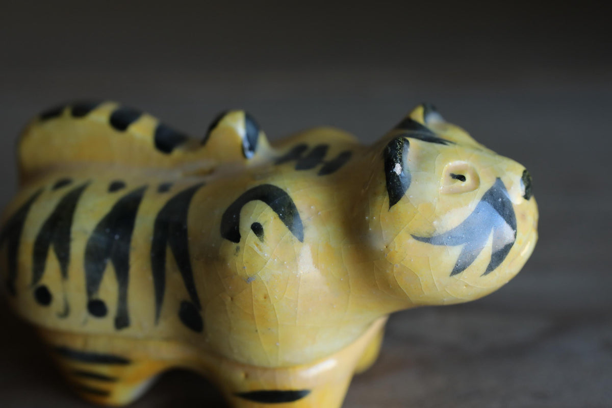 A close-up image of a yellow and black tiger figurine with a distinctive black stripe pattern on its face.