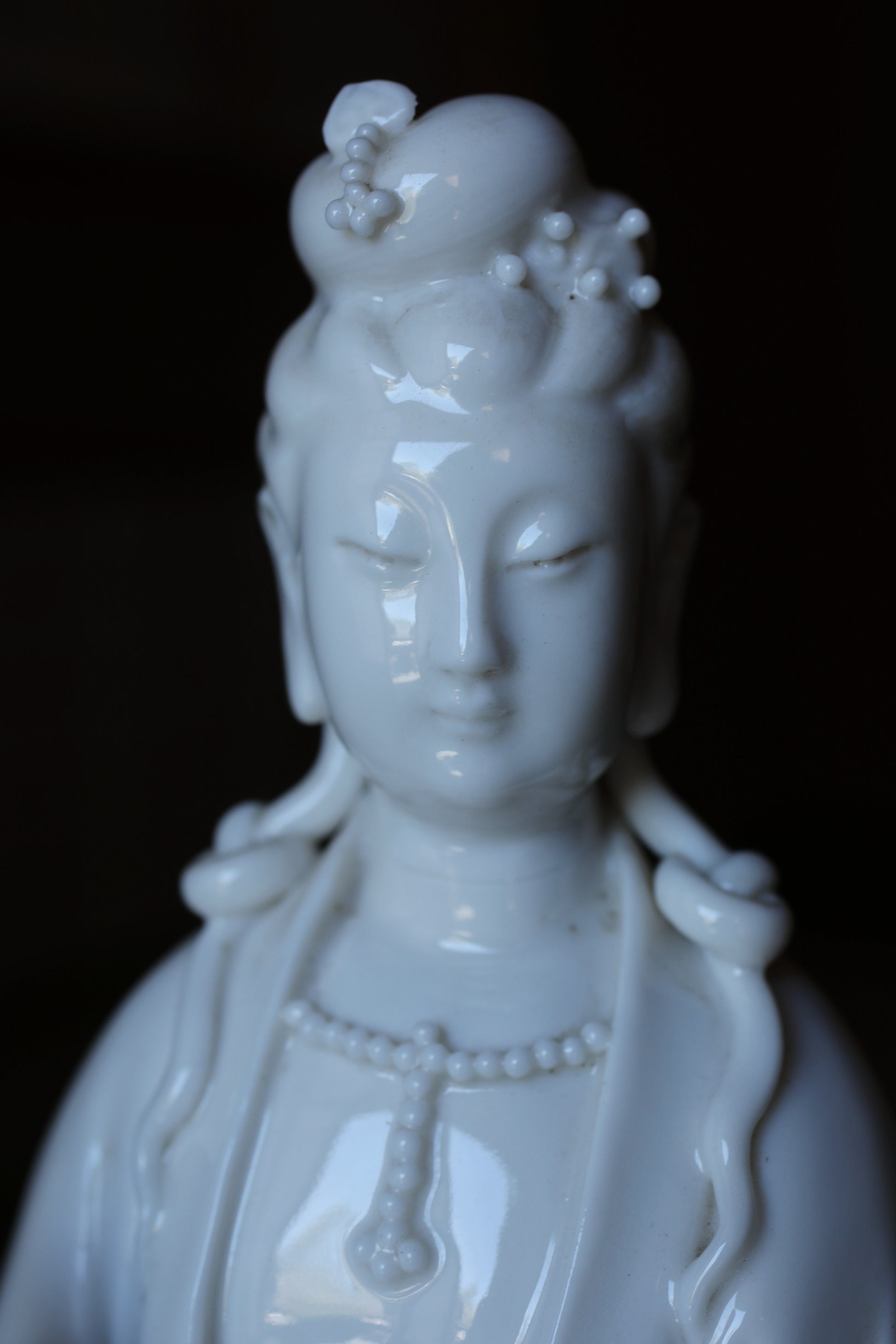 A close-up image of a white ceramic statue depicting a female deity with an ornate headdress and necklace.