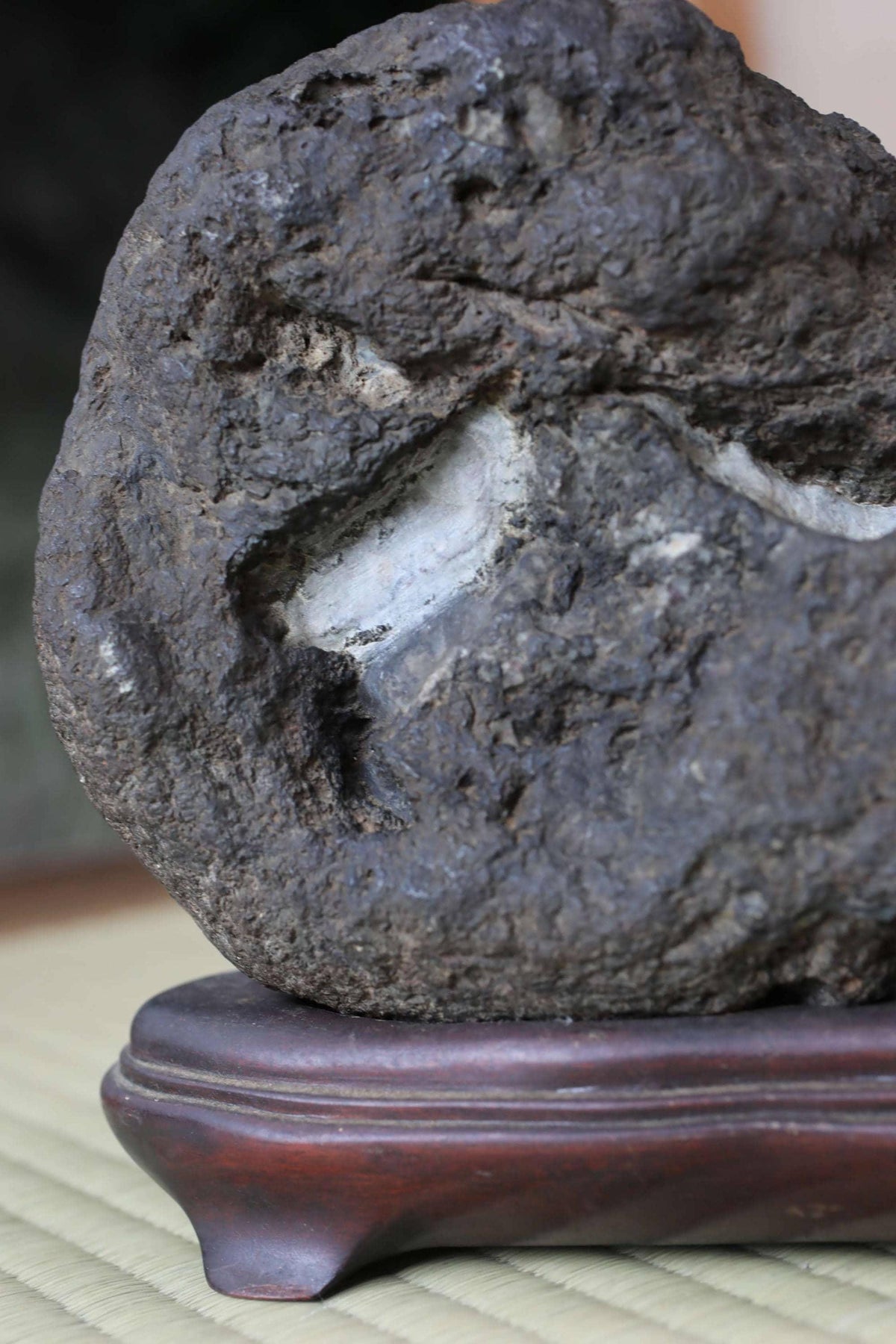 A large, dark rock with a hole in it, sitting on a wooden base.
