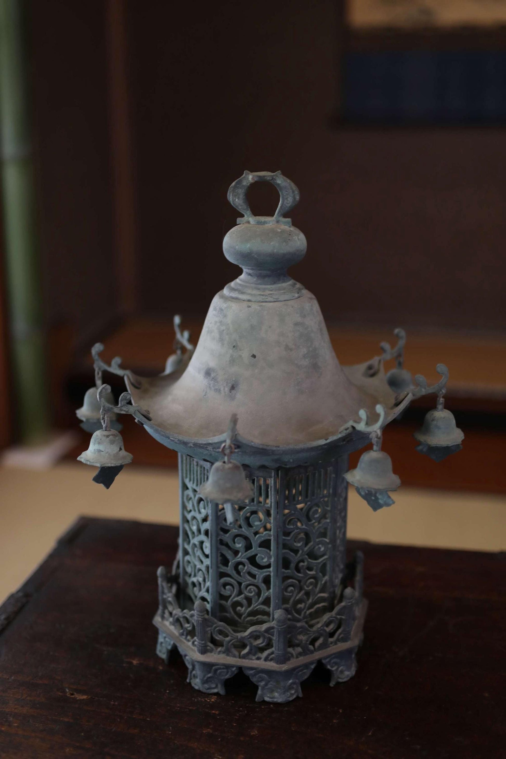 An antique metal lantern with a decorative design and hanging bells, sitting on a wooden surface.